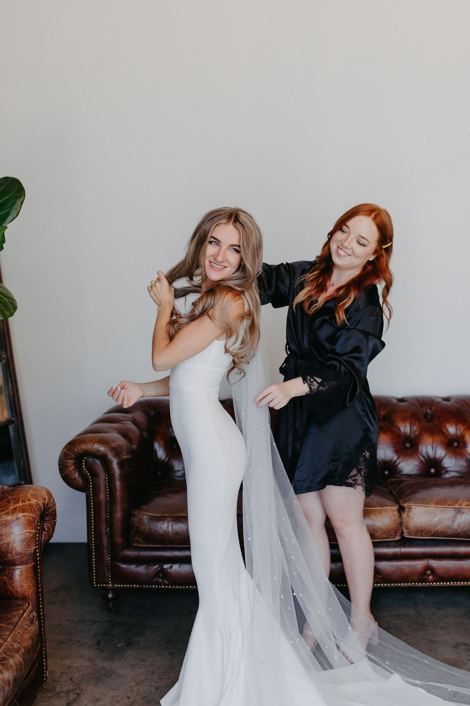 A wedding preparation scene with two people posing playfully against leather furniture.