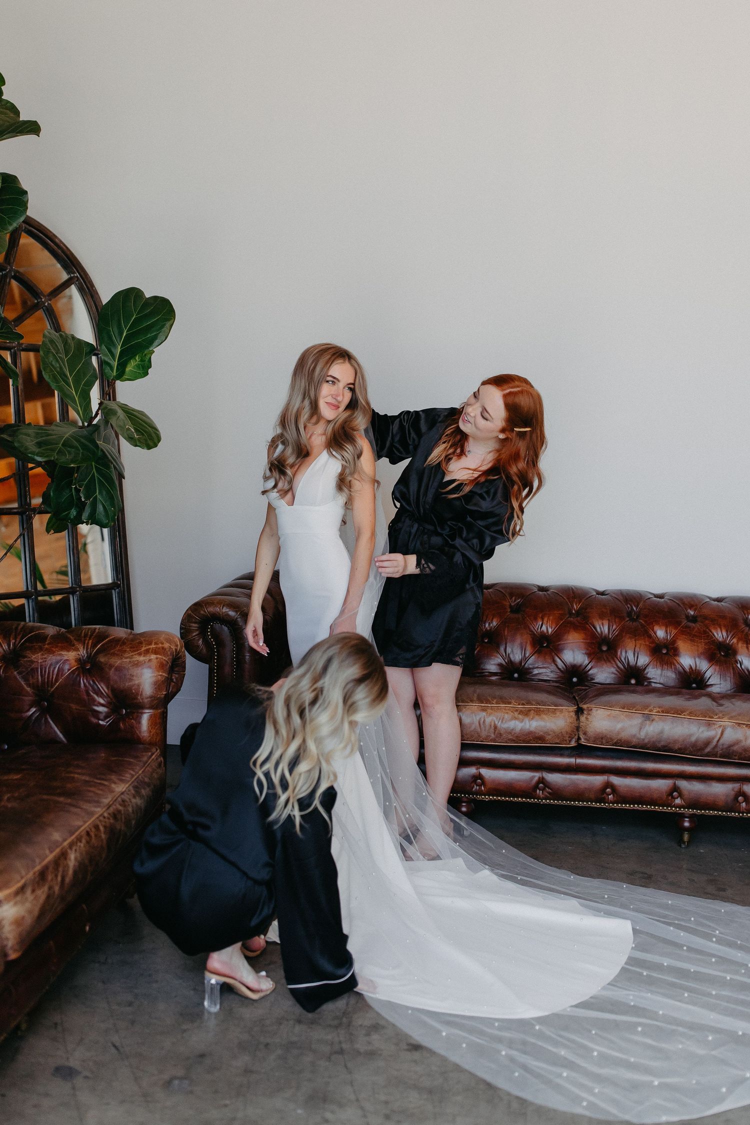 A bridal preparation scene with three people arranging a long wedding gown train.