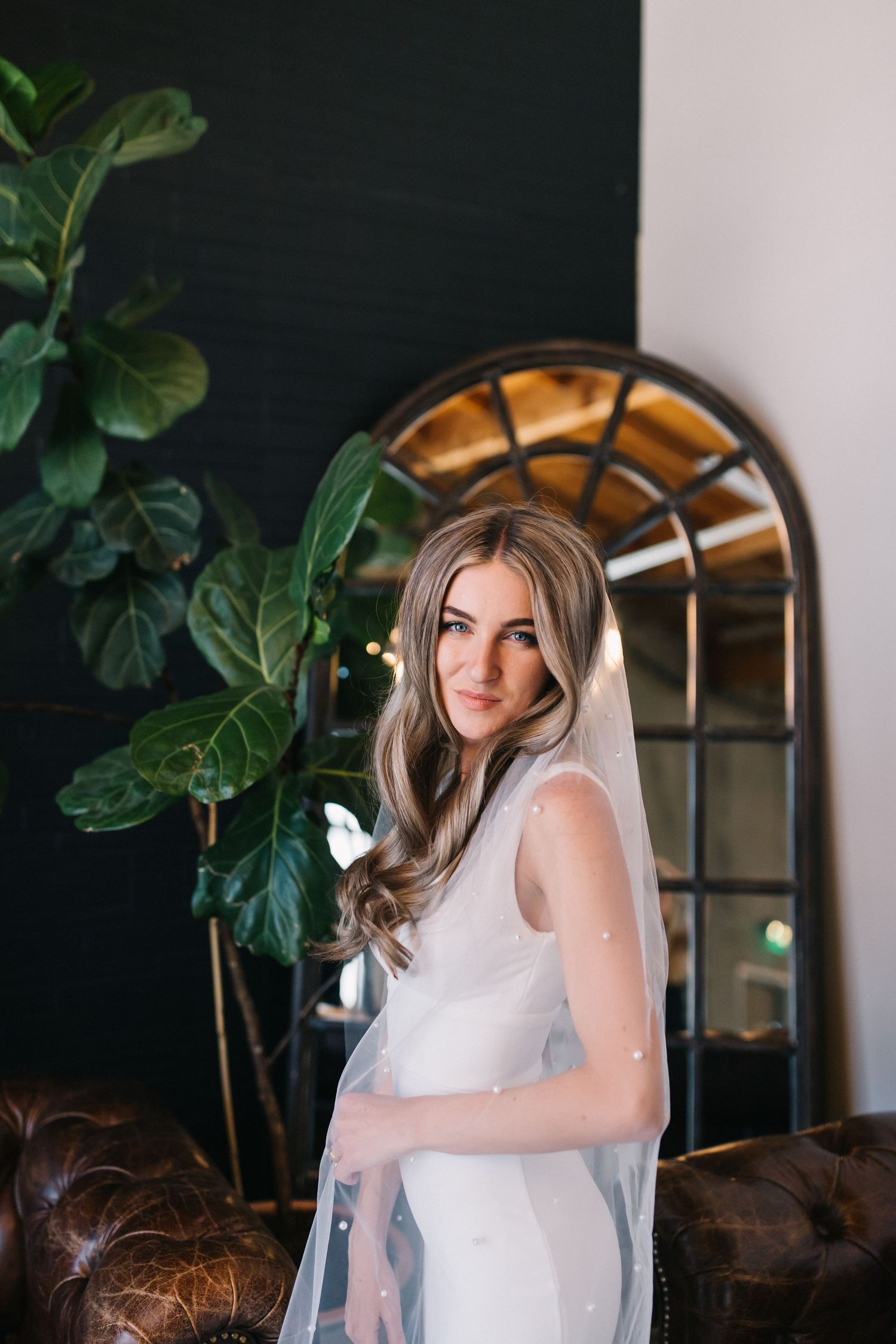 A elegant bridal portrait beside an arched mirror and fiddle leaf fig plant.