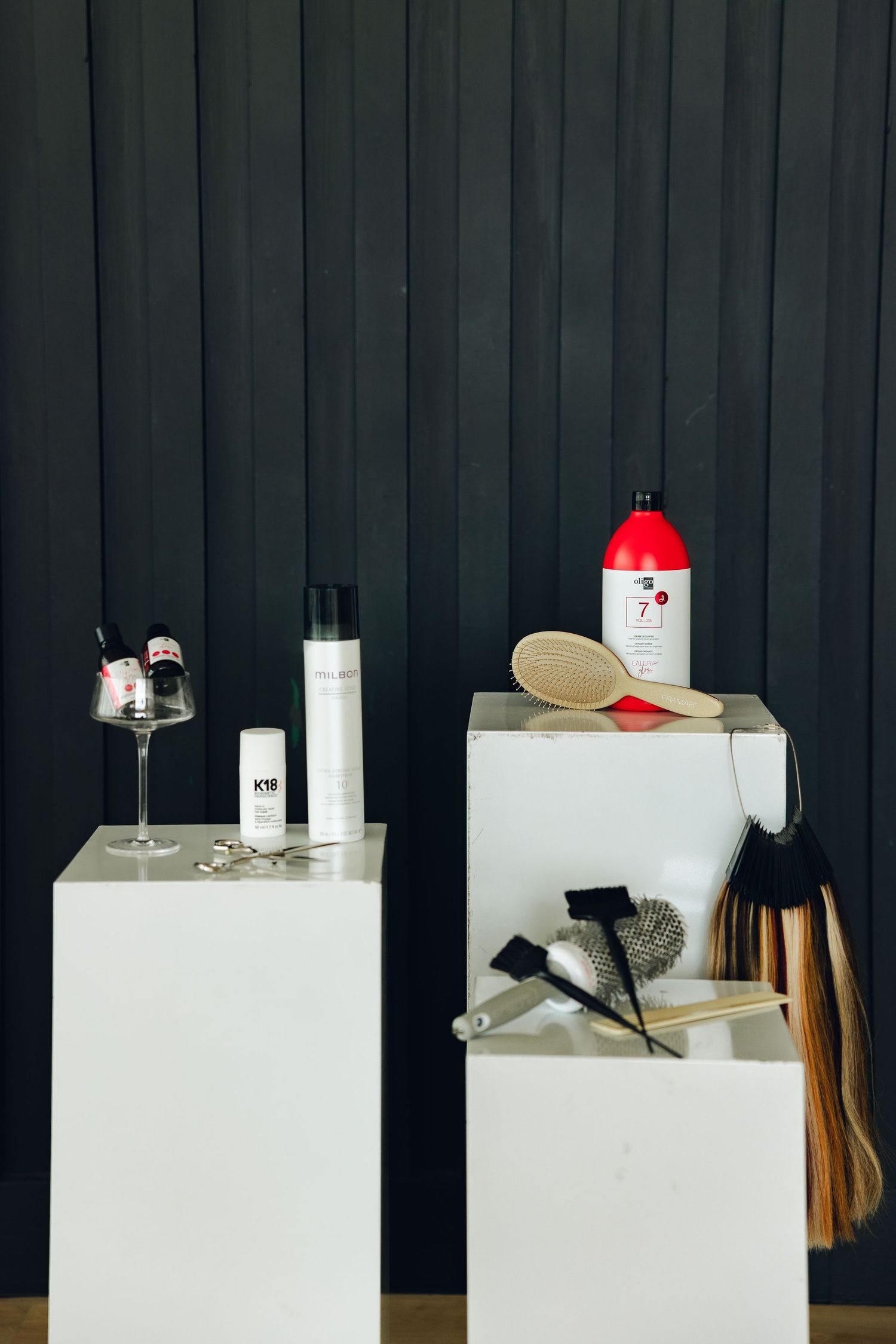 Minimalist still life composition with white pedestals displaying various objects against a dark striped background.
