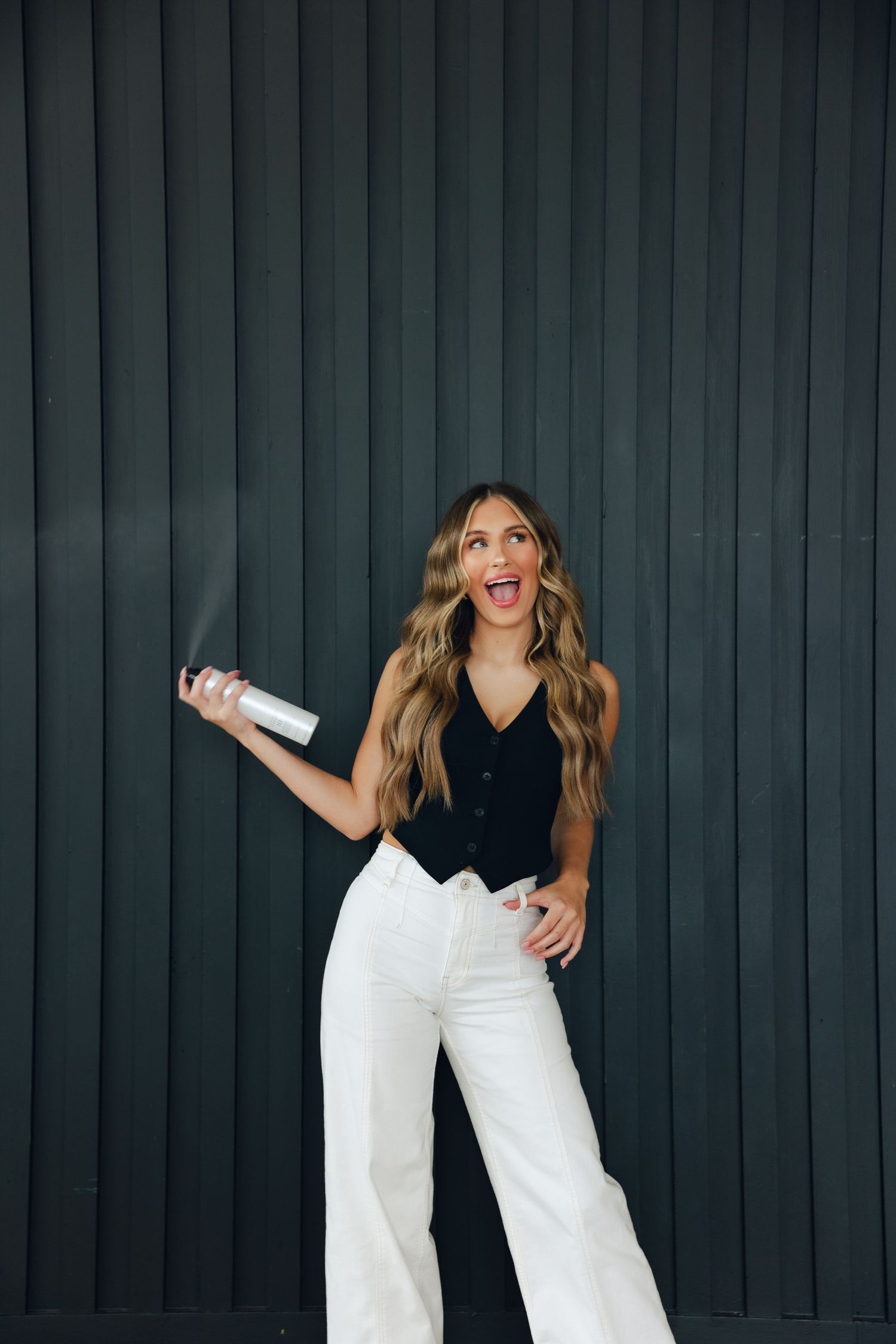 A woman in white pants poses playfully in four different poses against a dark wall background.