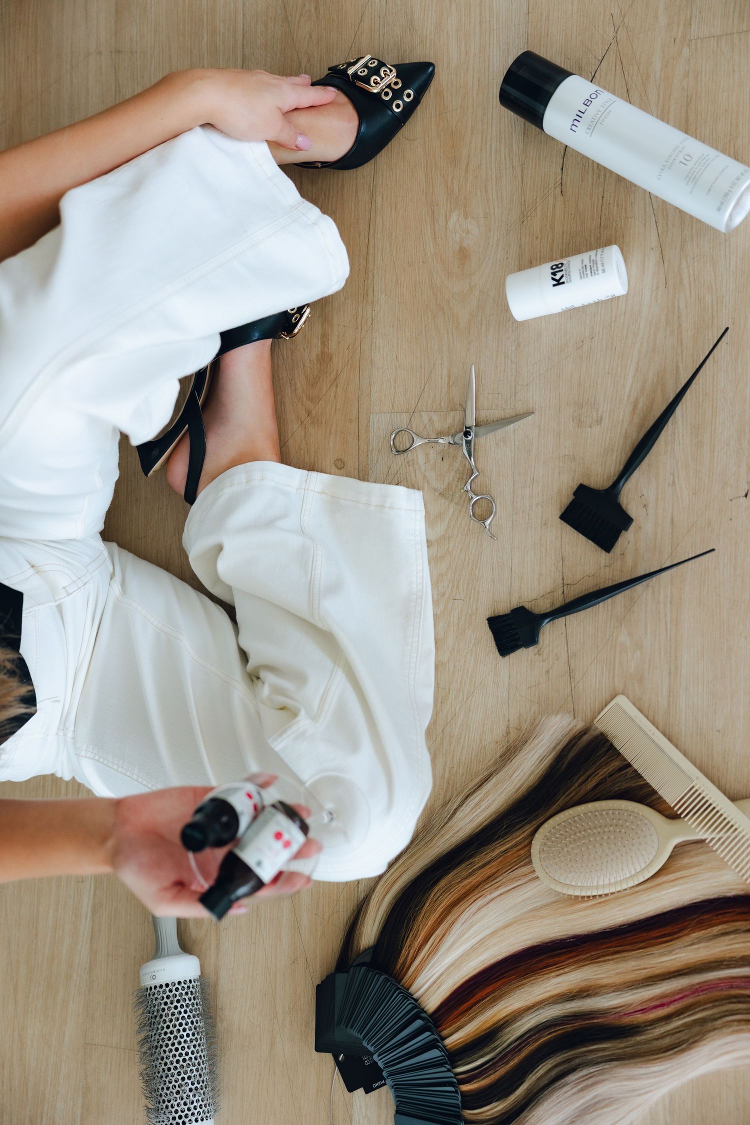 Hair styling tools and accessories laid out on wooden surface showing step-by-step hair extension application process.