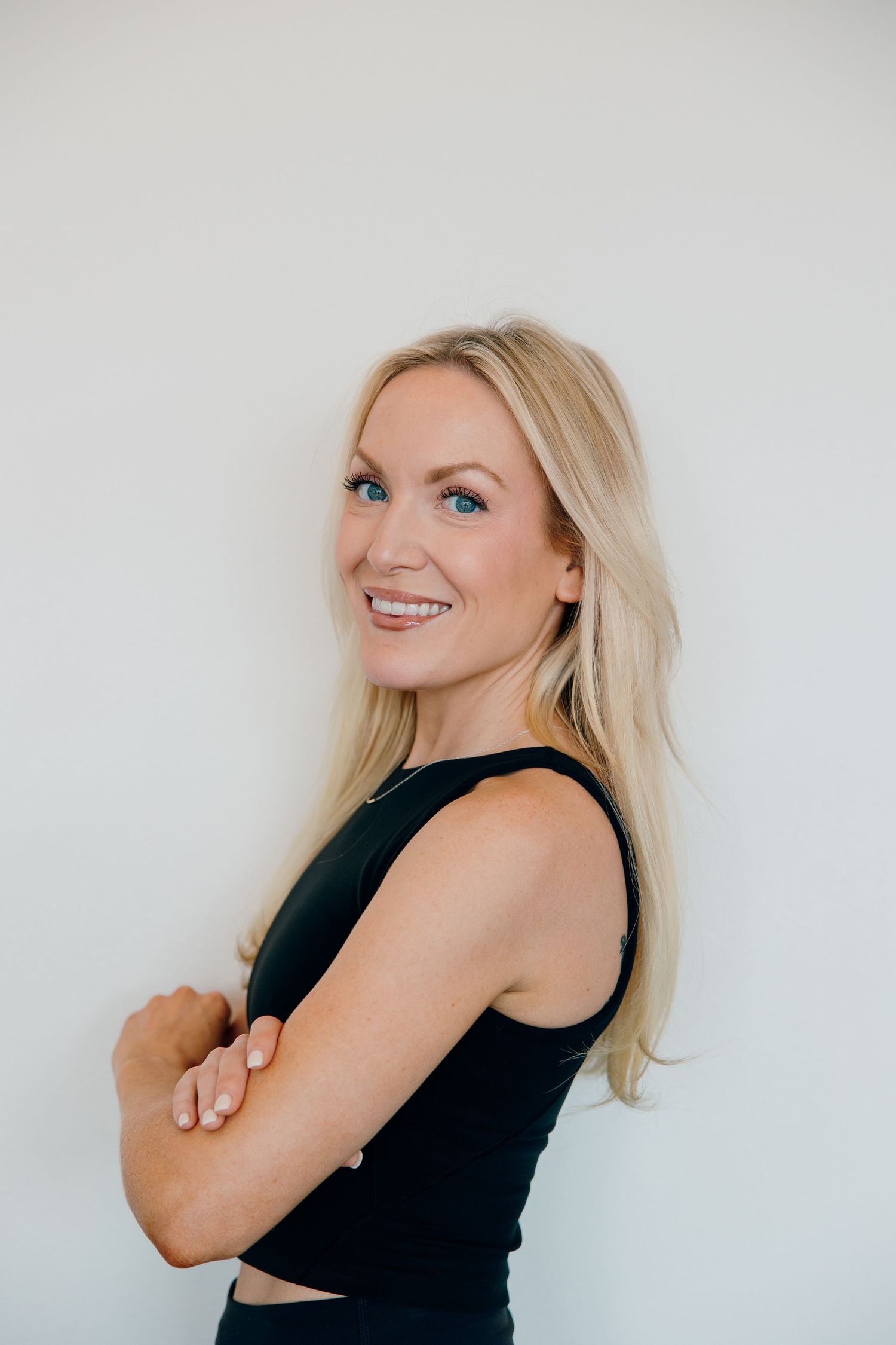 Professional portrait of a blonde woman in a black sleeveless top smiling against a white background.