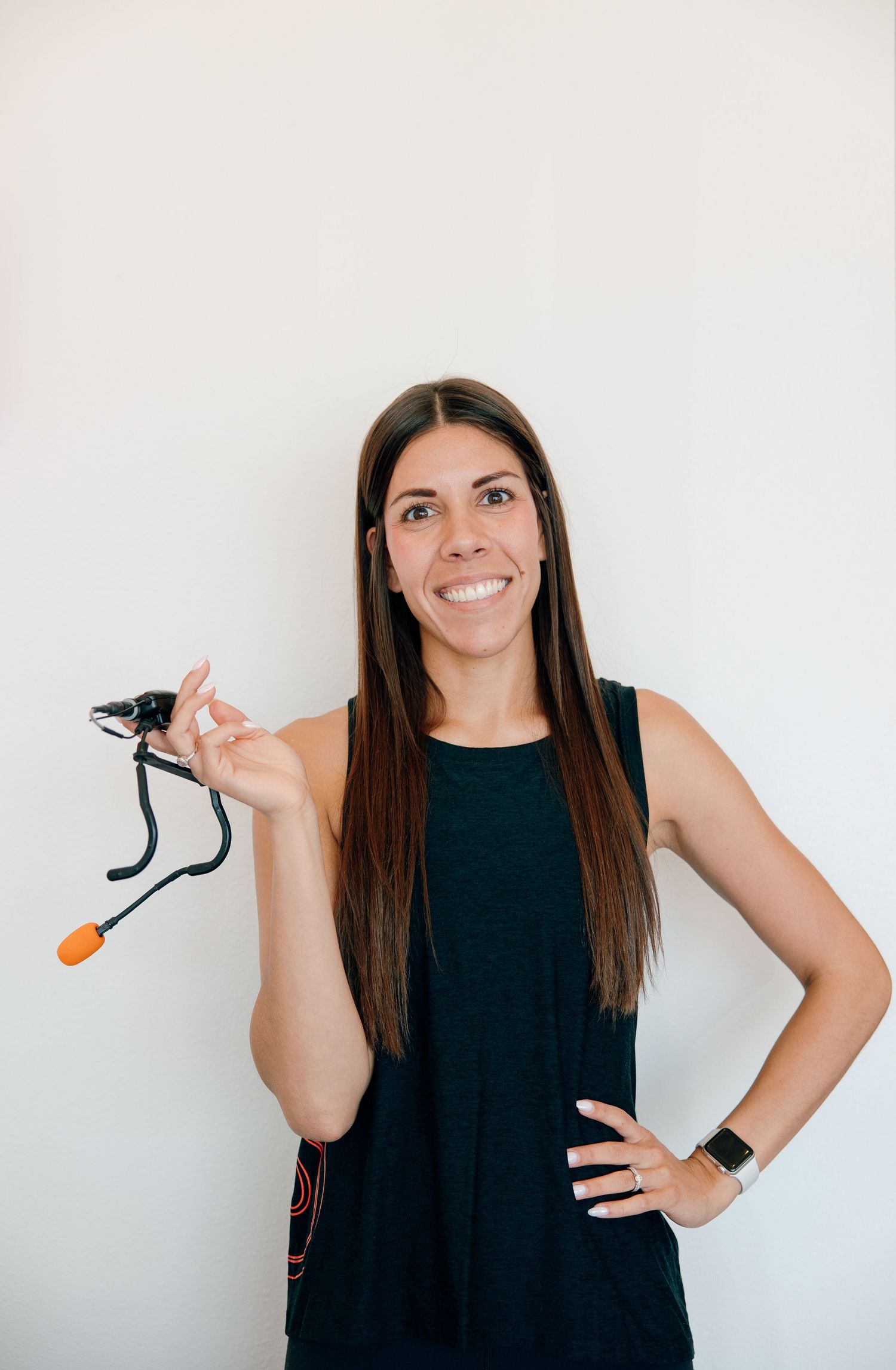 Person in a black sleeveless top poses against white wall while holding clothes hanger.