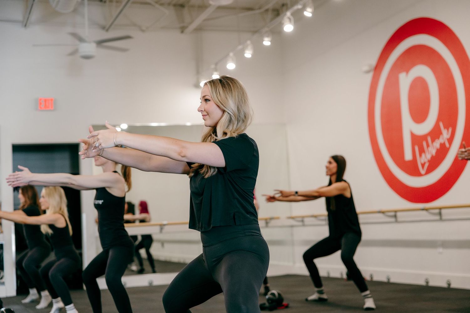 People exercising in a group fitness class with Pure Barre branding visible on the wall in a bright studio space.