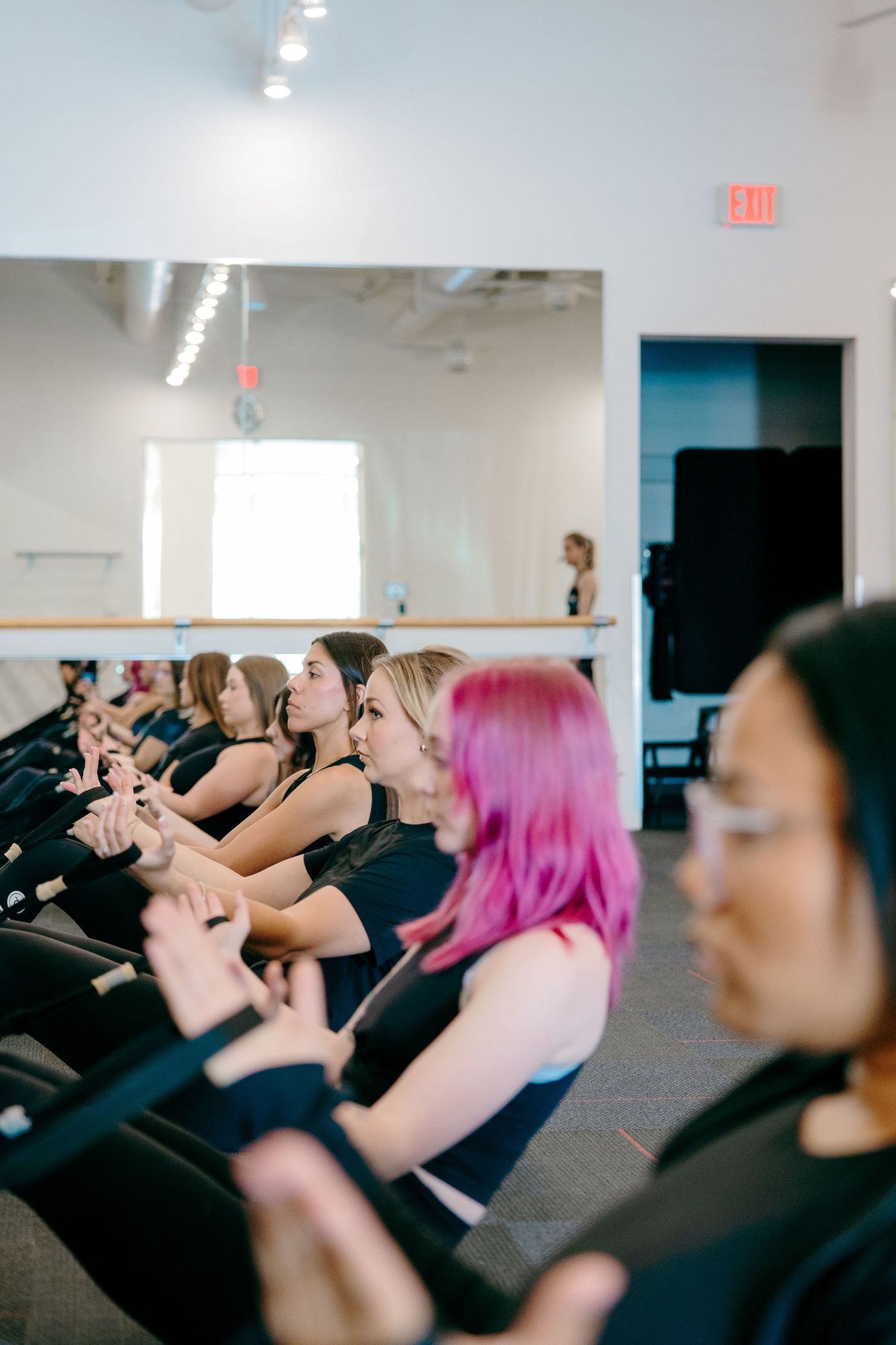 Group fitness class participants sitting in rows during an exercise session in a bright studio space.