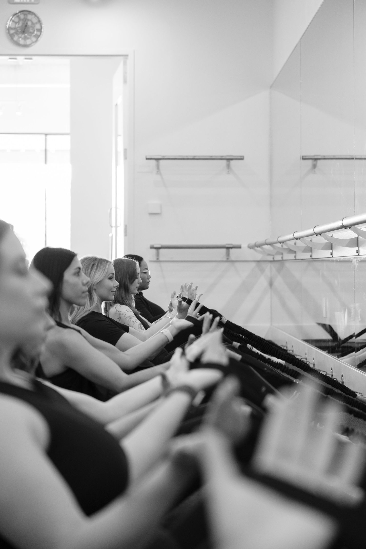 Students at a barre fitness class use exercise risers while facing sideways during a workout session.