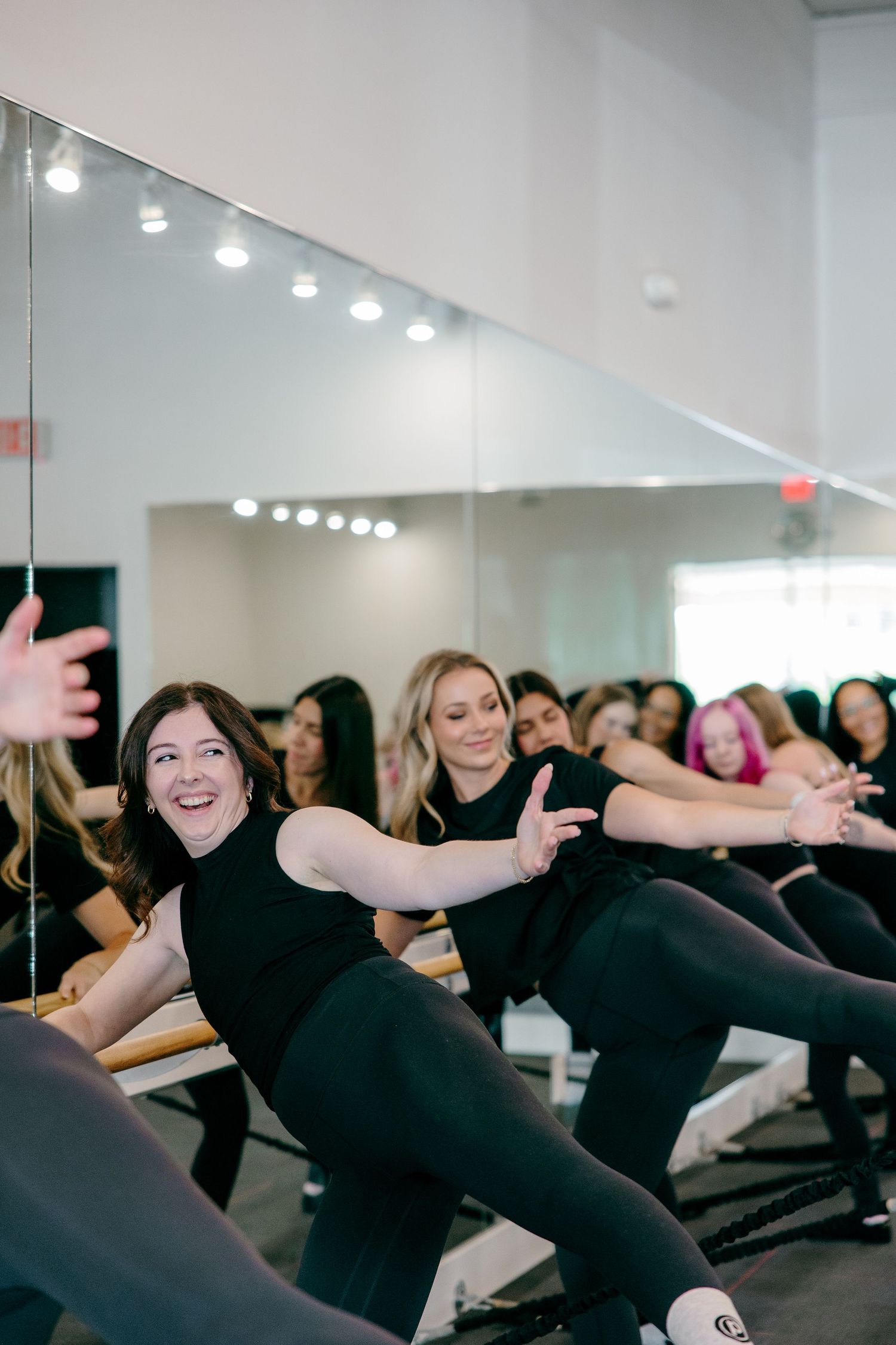 Group fitness class participants performing synchronized stretching exercises in a bright studio.