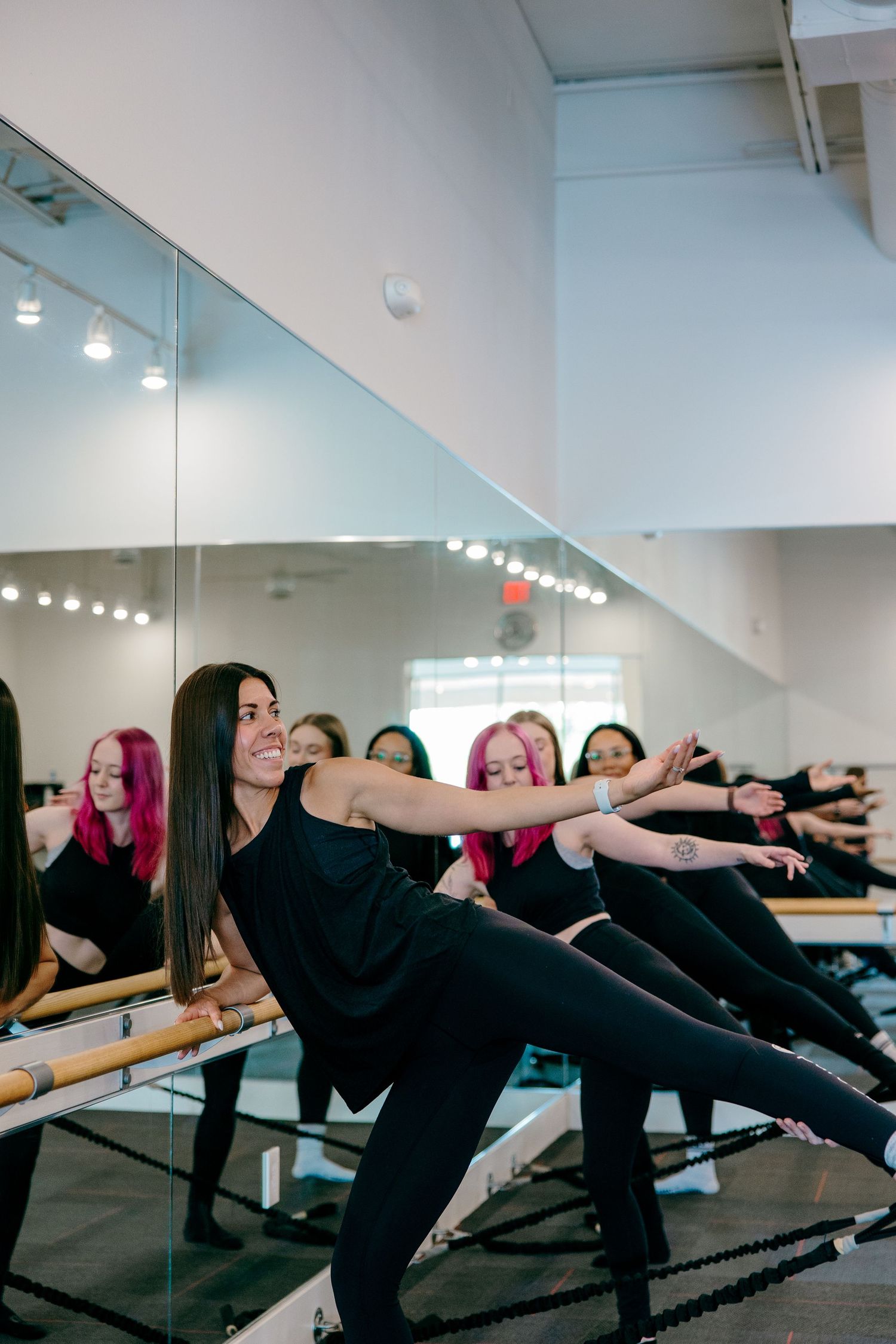 Fitness class participants perform leg extensions at a mirrored workout studio with track lighting.