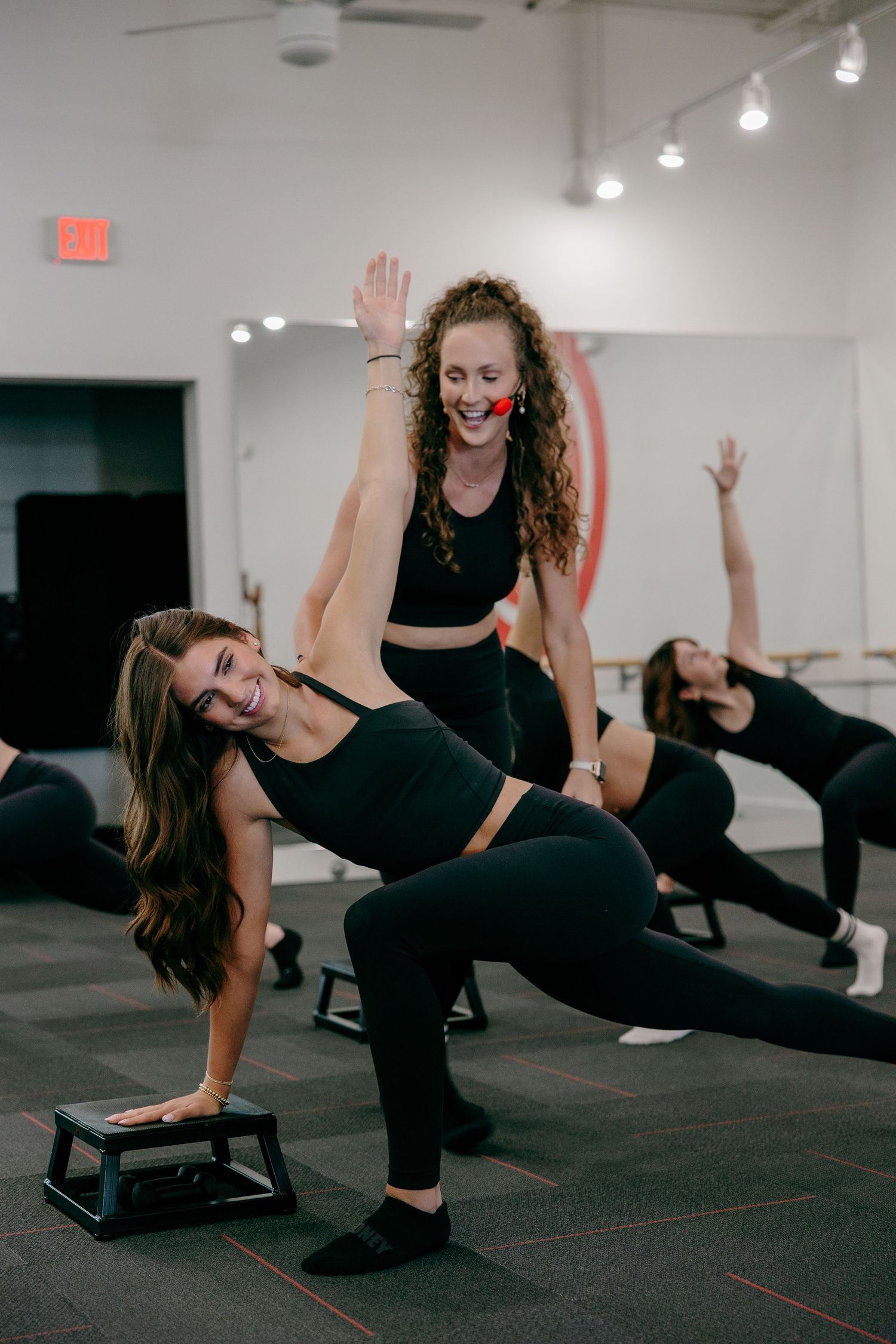 Group of people performing side plank exercises in a fitness studio with black floors and white walls.