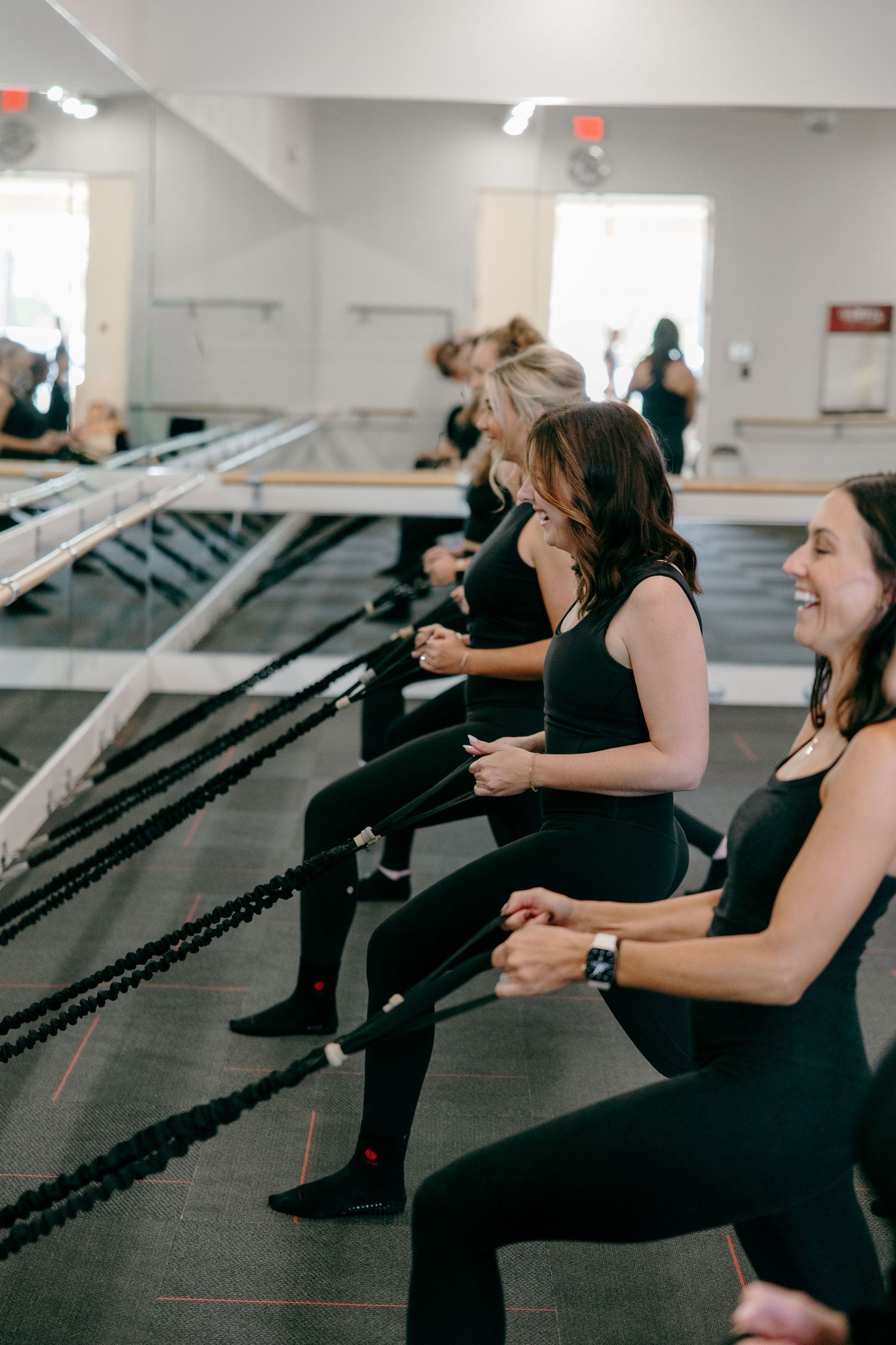 People in black workout attire exercising together at a fitness studio with reformer machines.