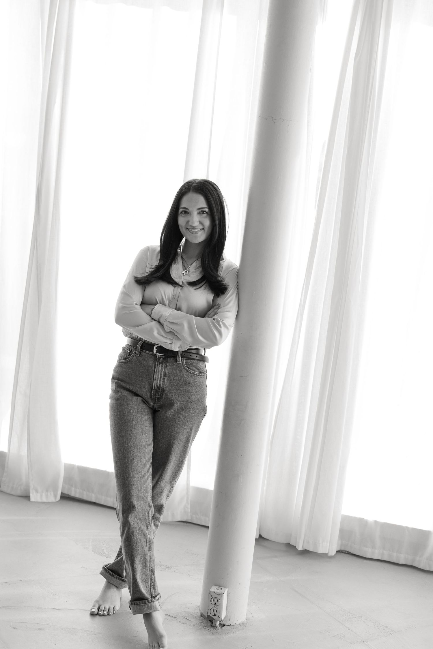 Black and white portrait of woman in casual attire leaning against white column.