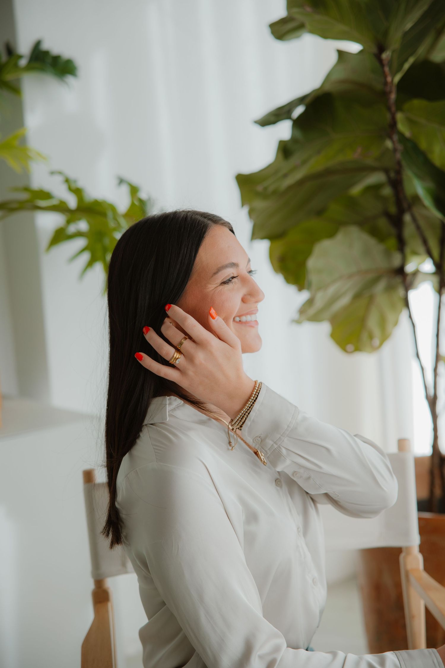 Woman in white shirt laughing by fiddle leaf fig plant in bright interior.