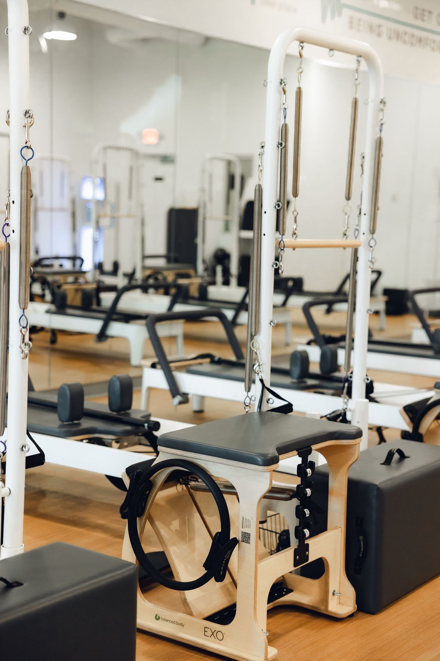 Modern Pilates studio interior with multiple reformer machines and equipment arranged in neat rows on wooden floors.