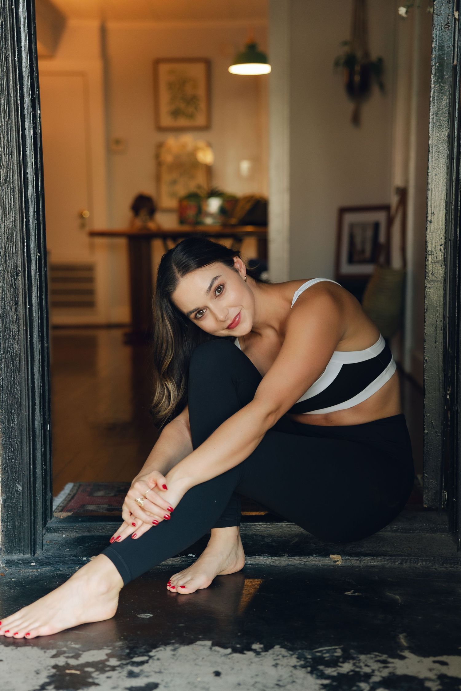 Woman in black workout attire stretching on wooden floor in warm interior setting.
