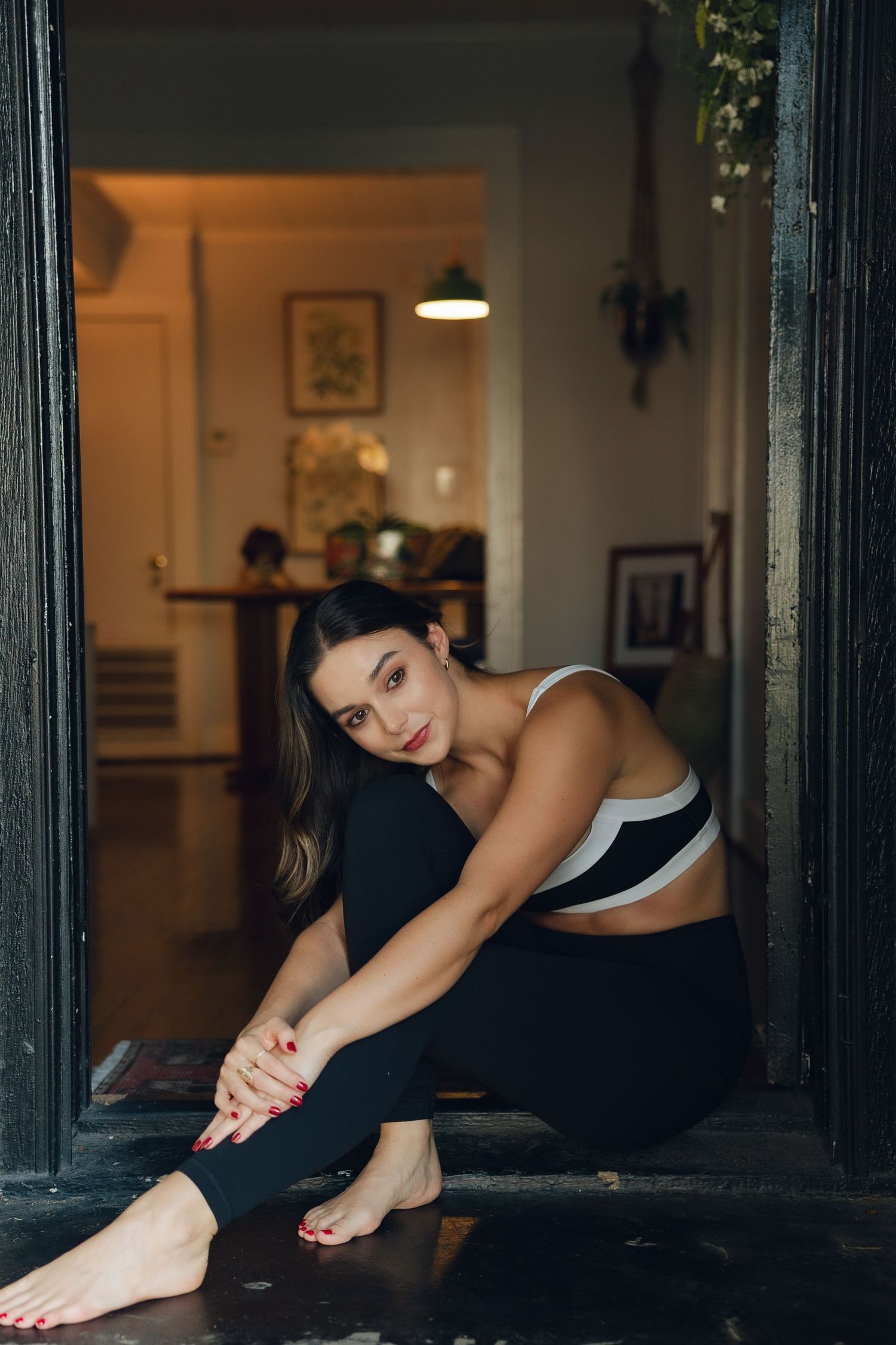 Woman in athletic wear doing stretching exercises on hardwood floor near window.