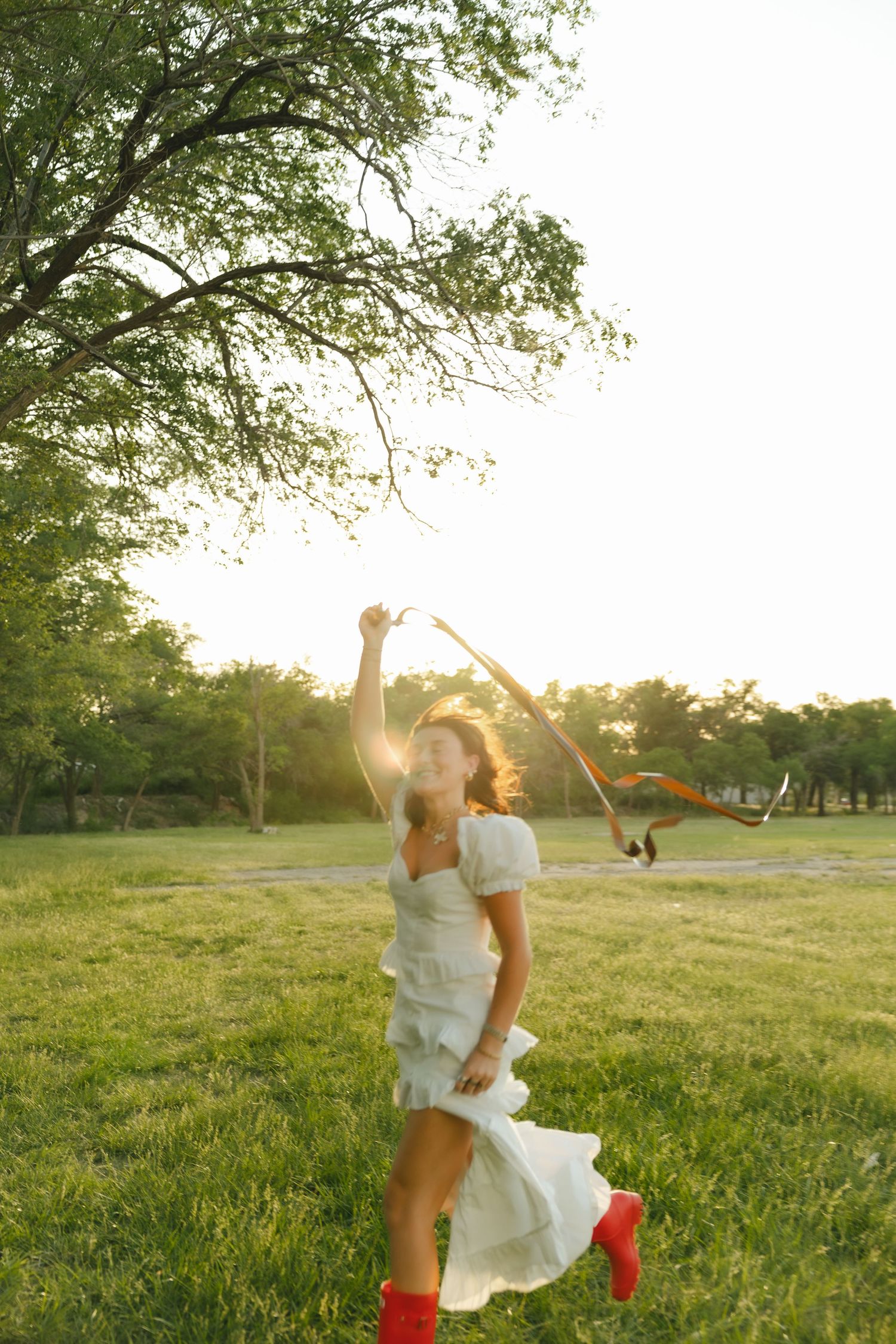 A person in a white dress dancing joyfully in a field at sunset while wearing vibrant red boots.