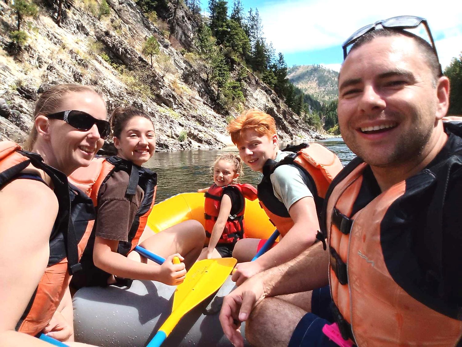 Group wearing life jackets enjoying time on a boat near mountainous shoreline.