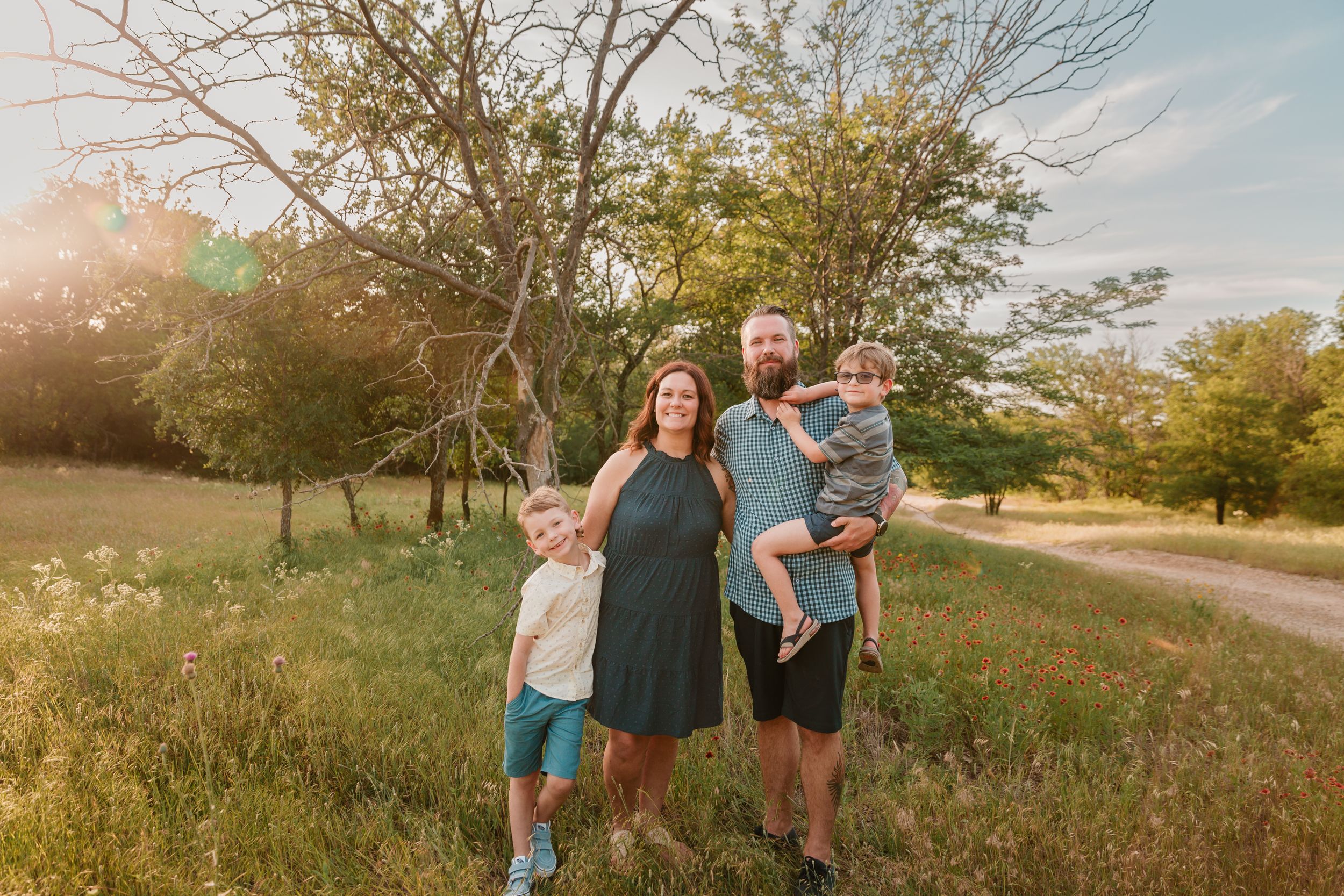 Family poses together at sunset in grassy field with trees in background.