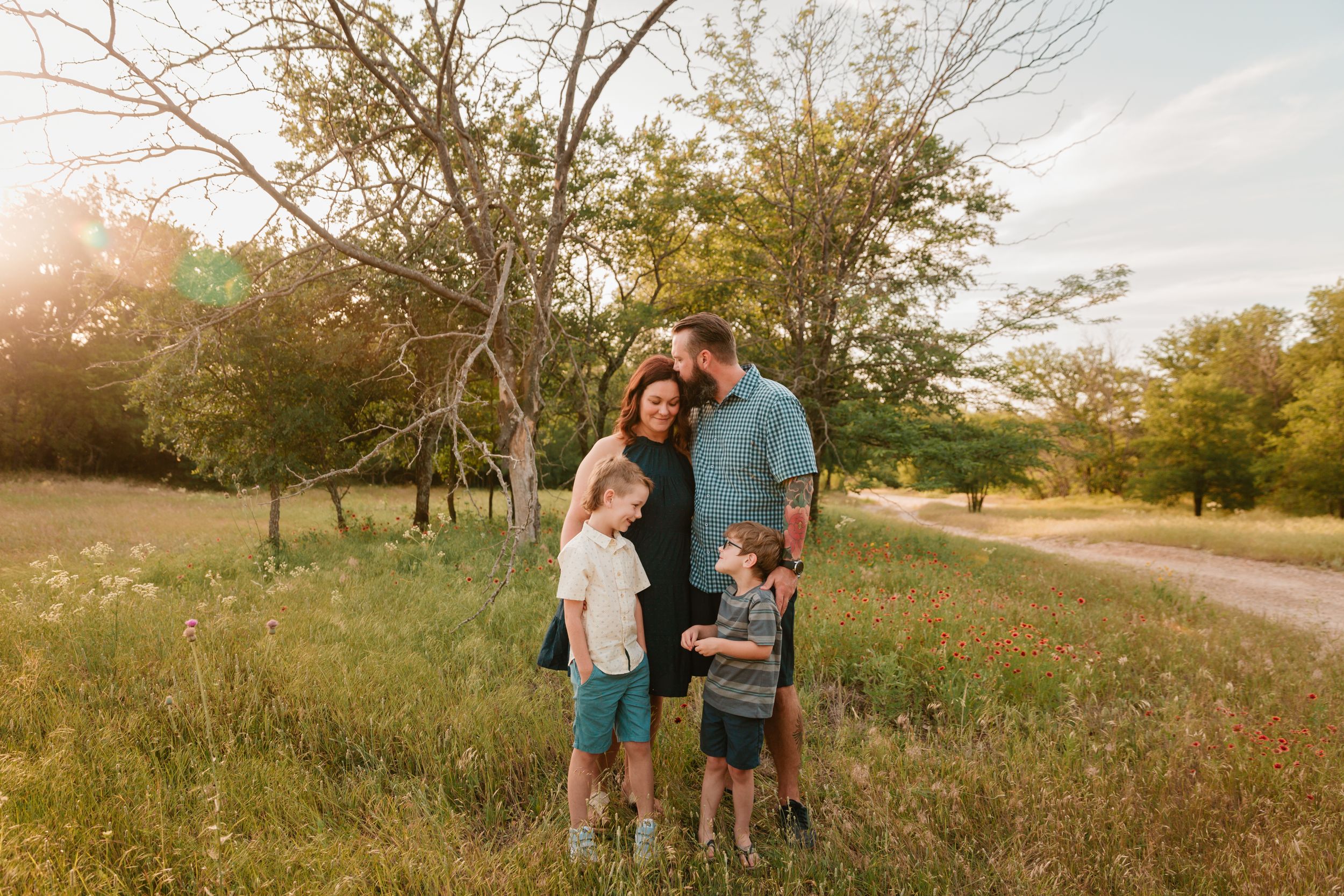 Family stands together in golden sunlight on dirt path near trees.