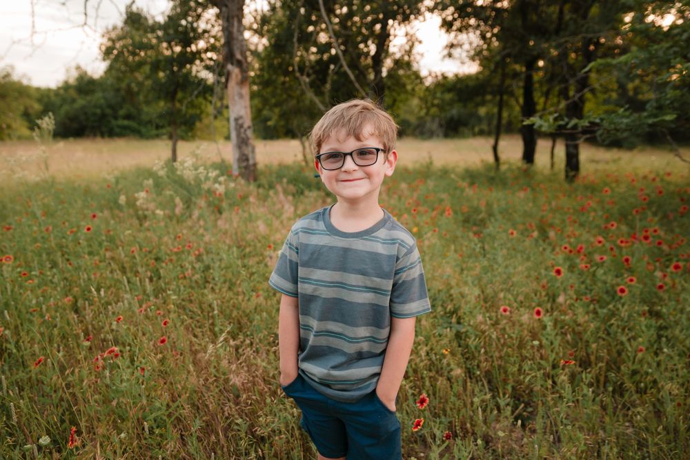Boy in a striped shirt adorned figure stands in a wildflower meadow at golden hour.
