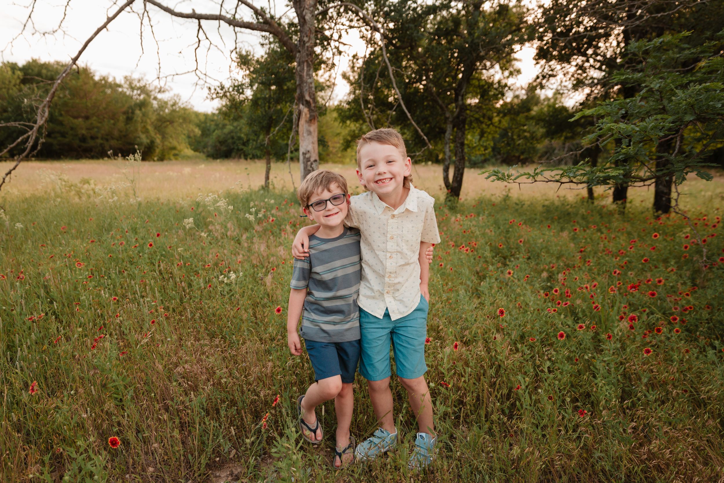 Brothers stand together in a wildflower field during sunset.