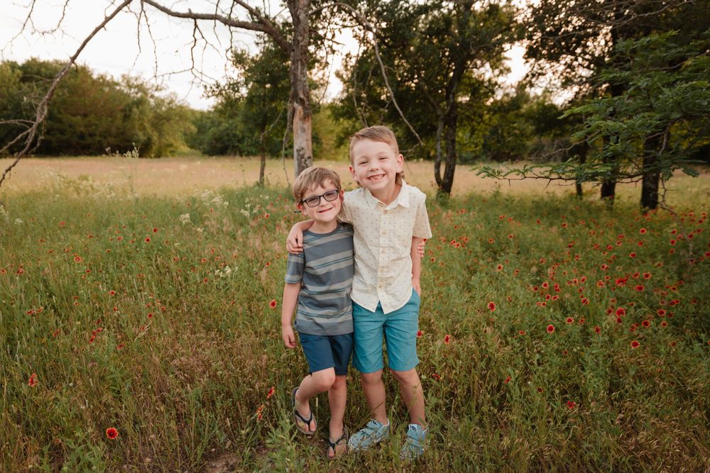 Brothers stand together in a wildflower field during sunset.
