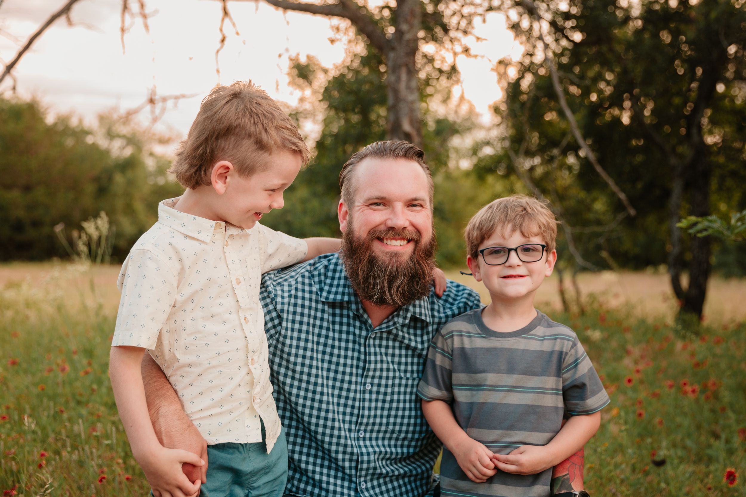 Dad and sons share a tender moment in a field dotted with red wildflowers.