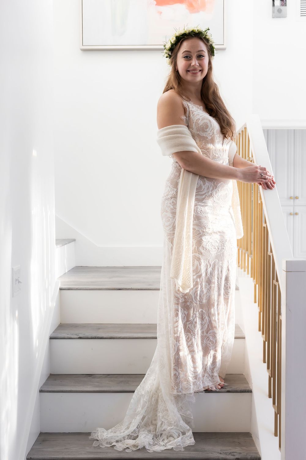 A person wearing a white lace wedding dress poses on stairs with golden railing.