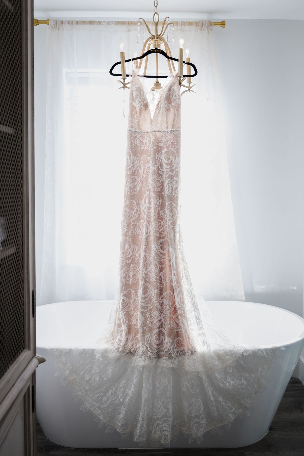 An elegant lace wedding dress hanging on display against a white bathroom interior.