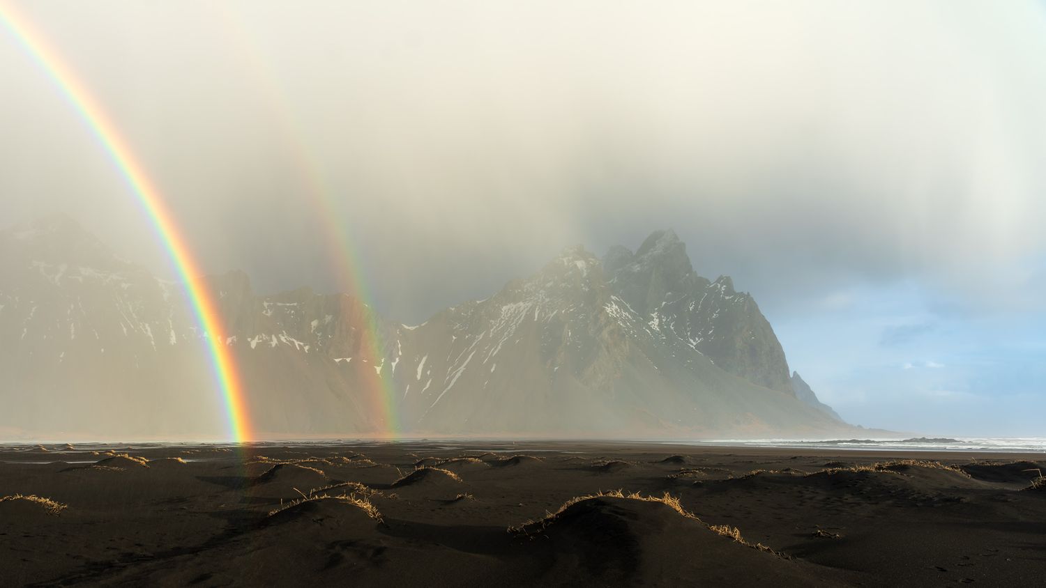 A double rainbow appears in front of Vestrahorn seeming to rise right out of the black sand beach.