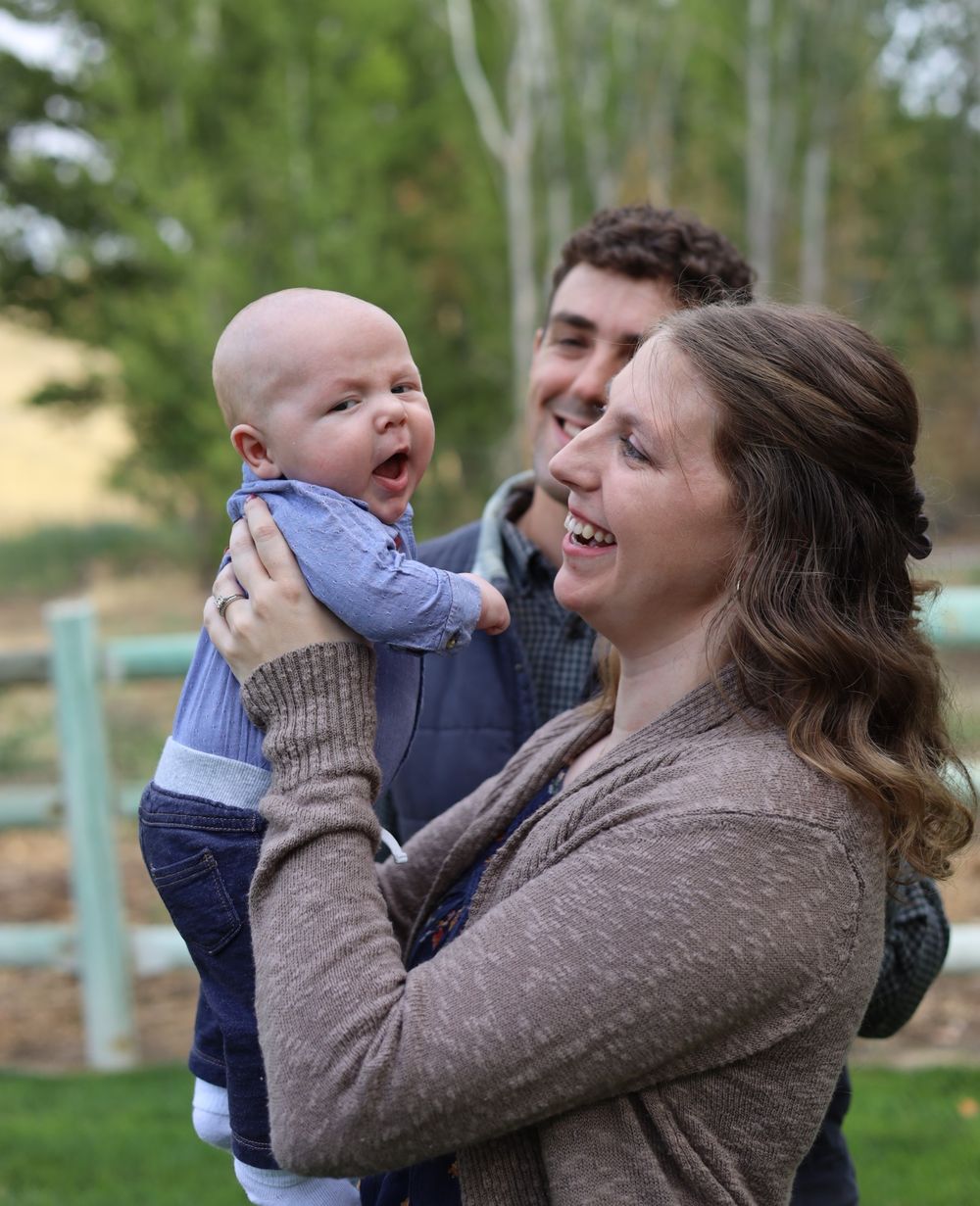 A joyful parent holds up their smiling baby while sharing an affectionate moment outdoors.
