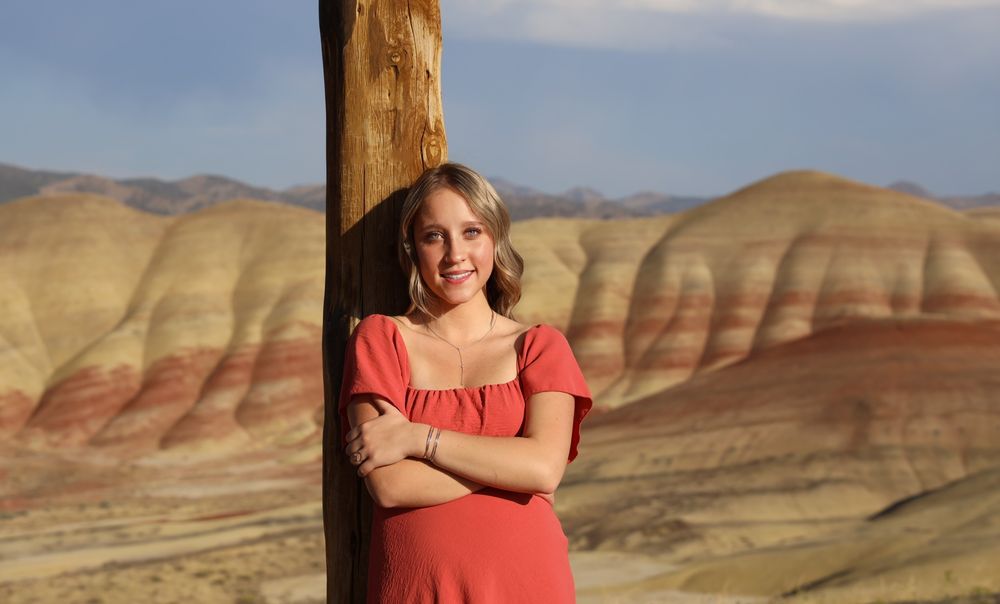 A person in a coral dress poses in front of the colorful Painted Hills of Oregon during golden hour.