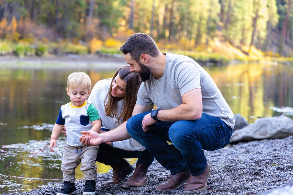 A family explores together by a serene lake surrounded by forest.