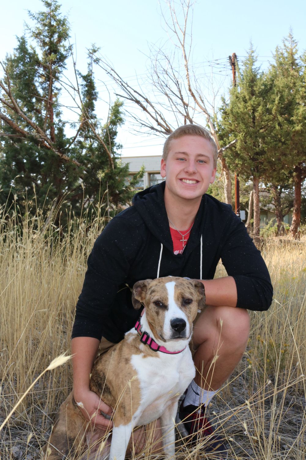 Person and friendly pit bull type dog posing together in natural outdoor setting.