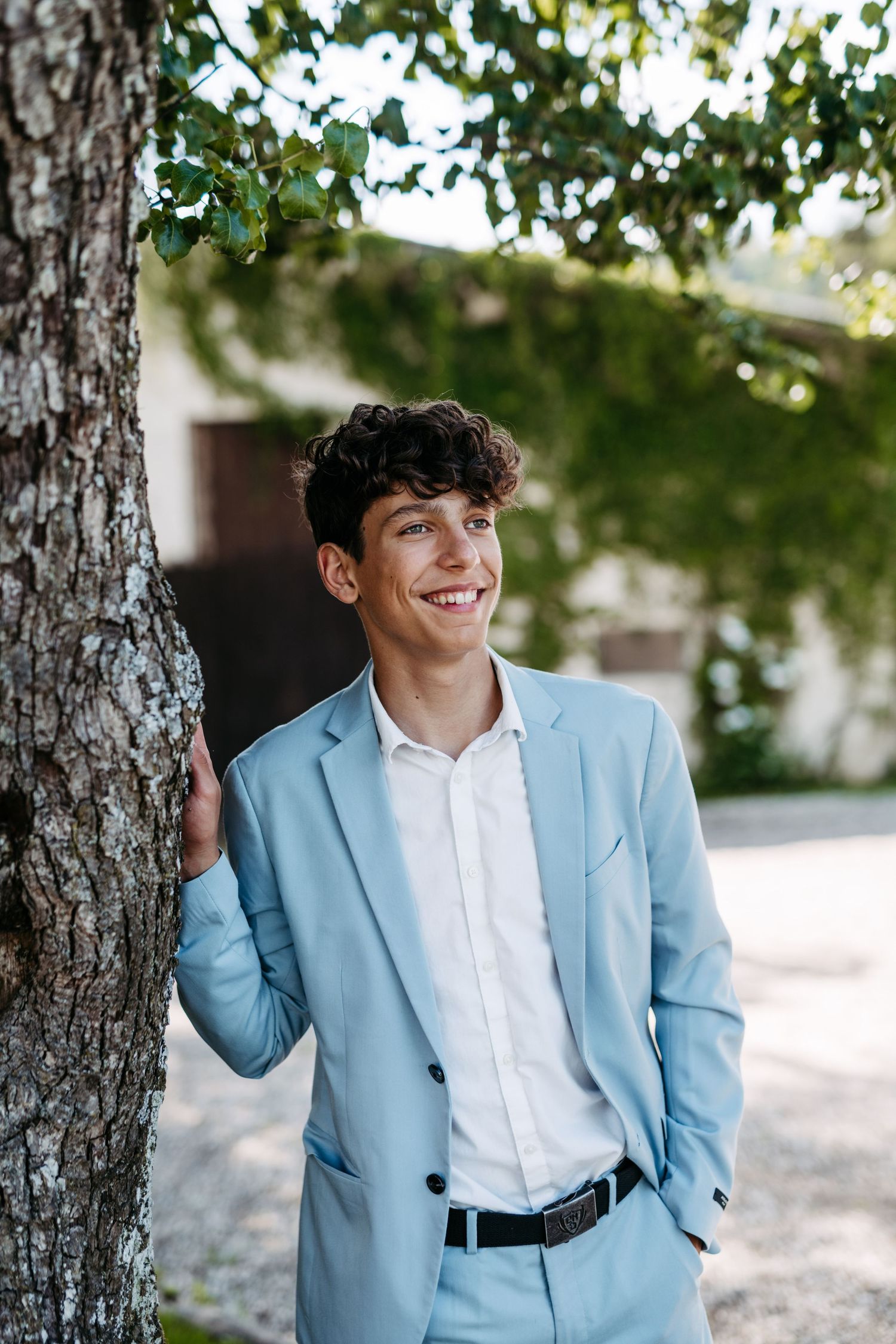 Casual fashion pose against a tree trunk wearing a contemporary light blue suit.