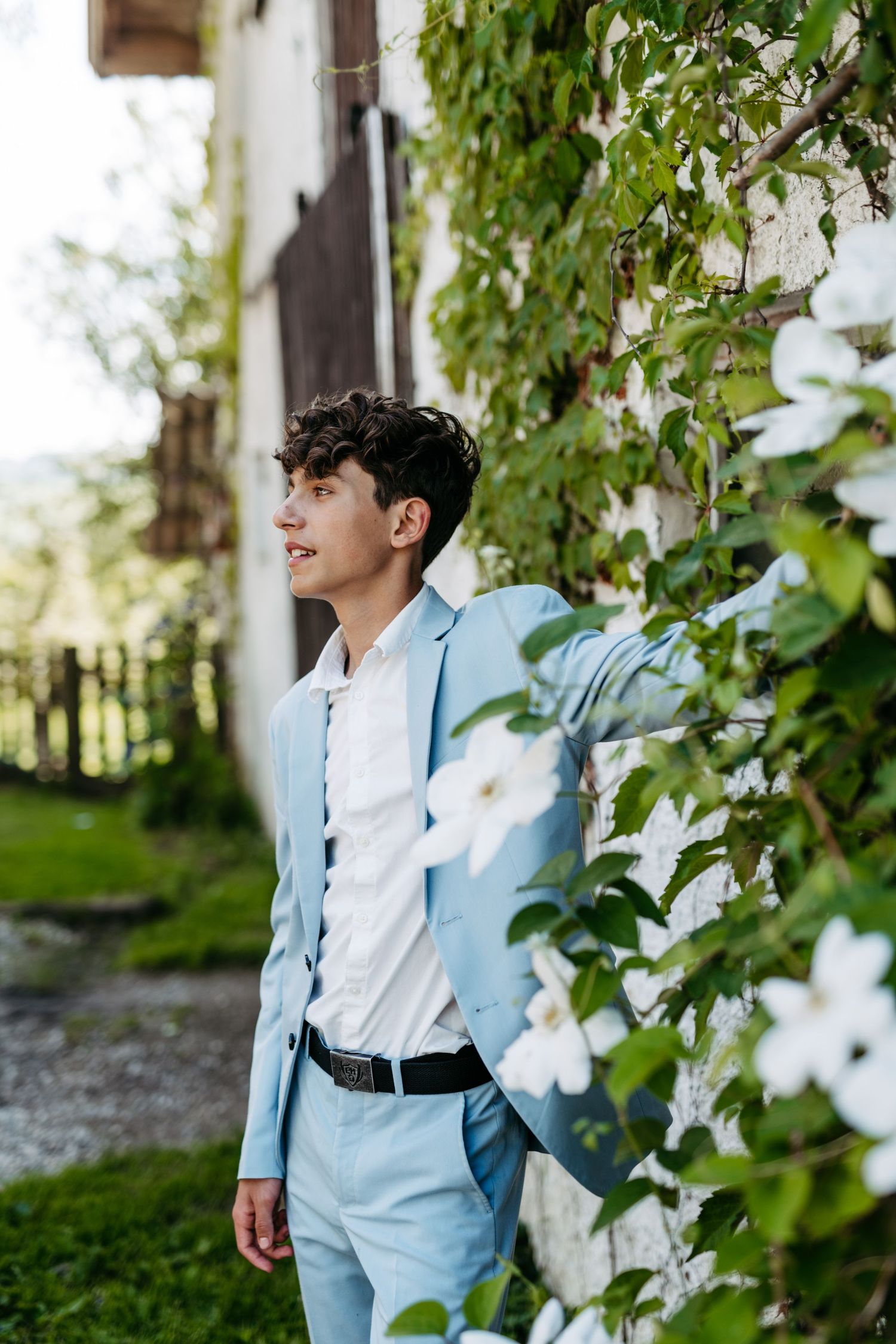Stylish light blue suit ensemble photographed against a lush garden backdrop with white flowers.