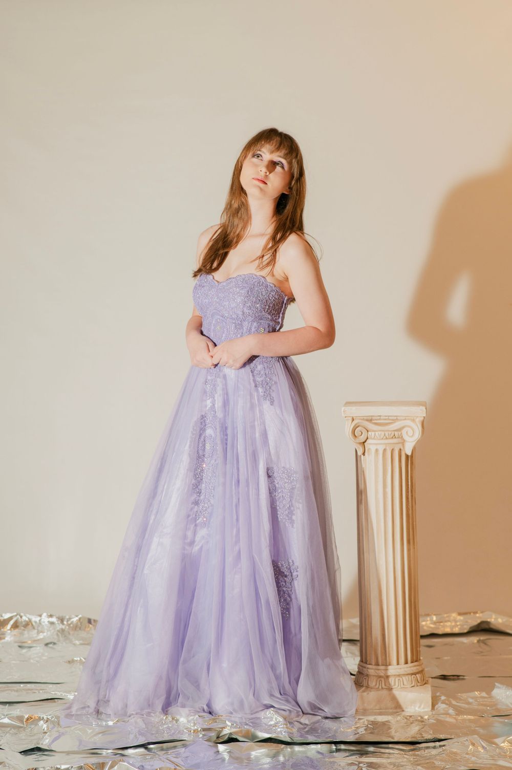 Elegant woman wearing a lavender strapless lace and tulle A-line prom gown standing by a white pillar.