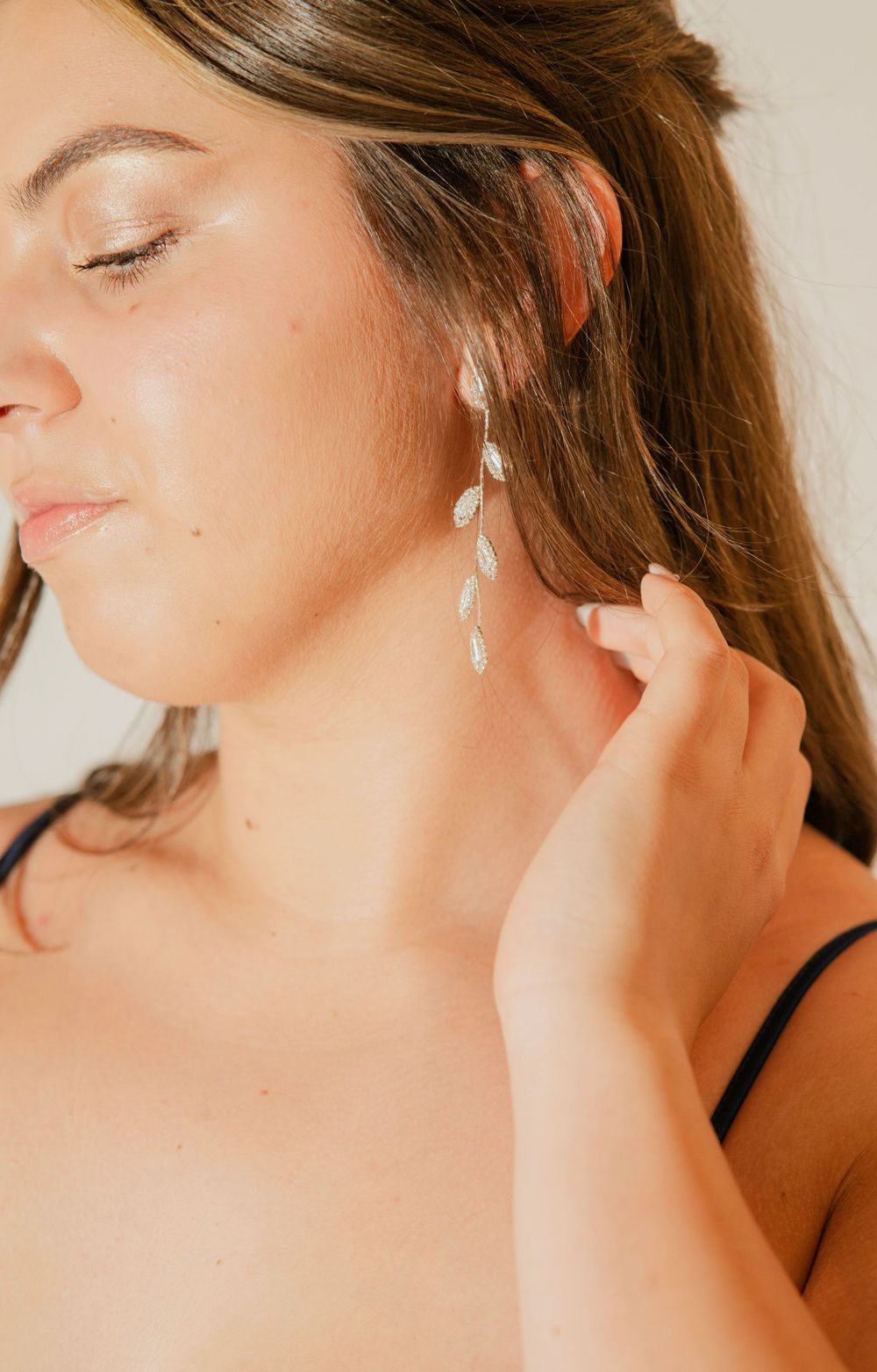 Close-up of woman wearing elegant silver drop leaf chandelier earrings with hand touching her ear.