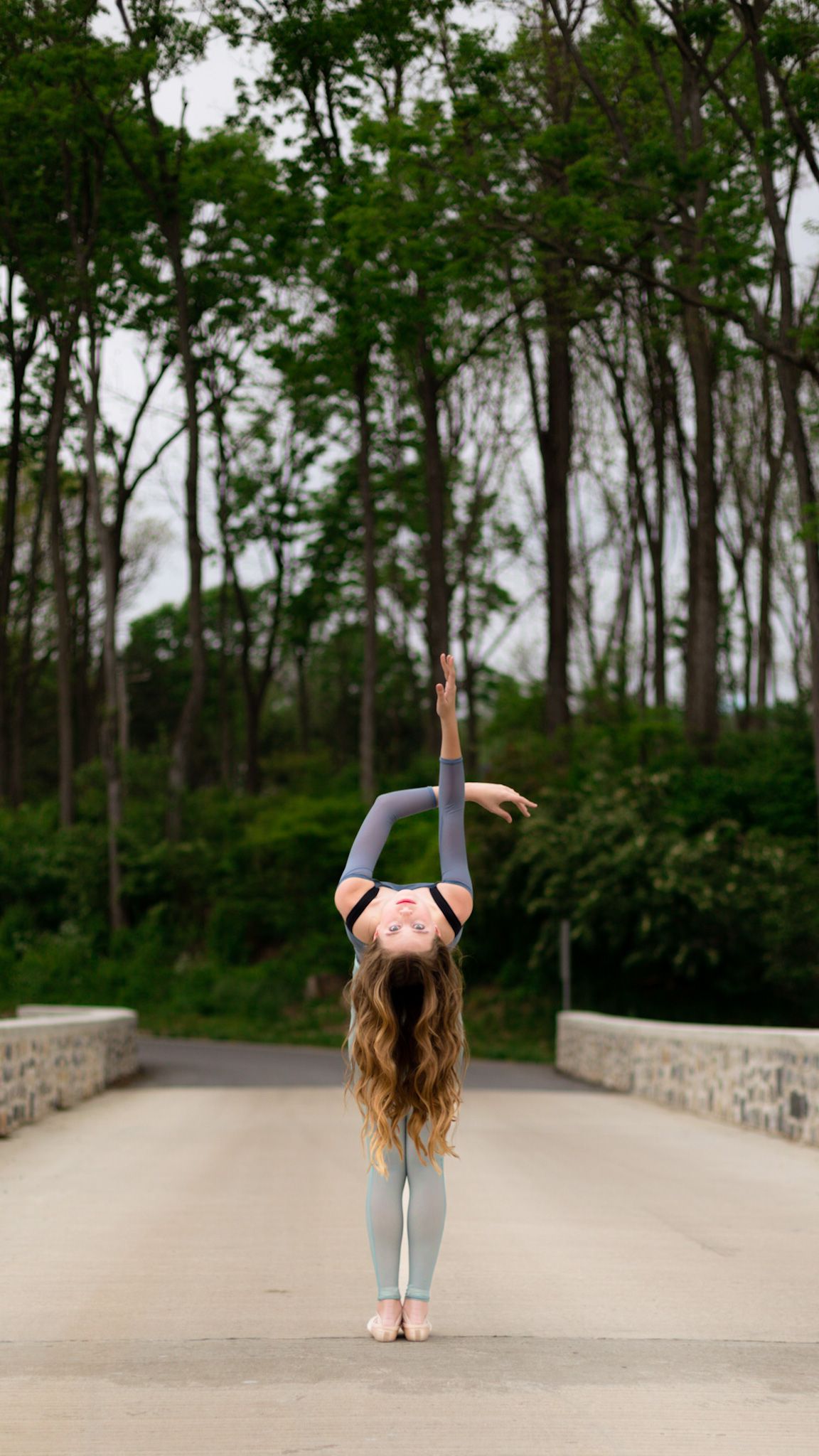 Dancer reaching skyward on a tree-lined bridge in Camp Hill