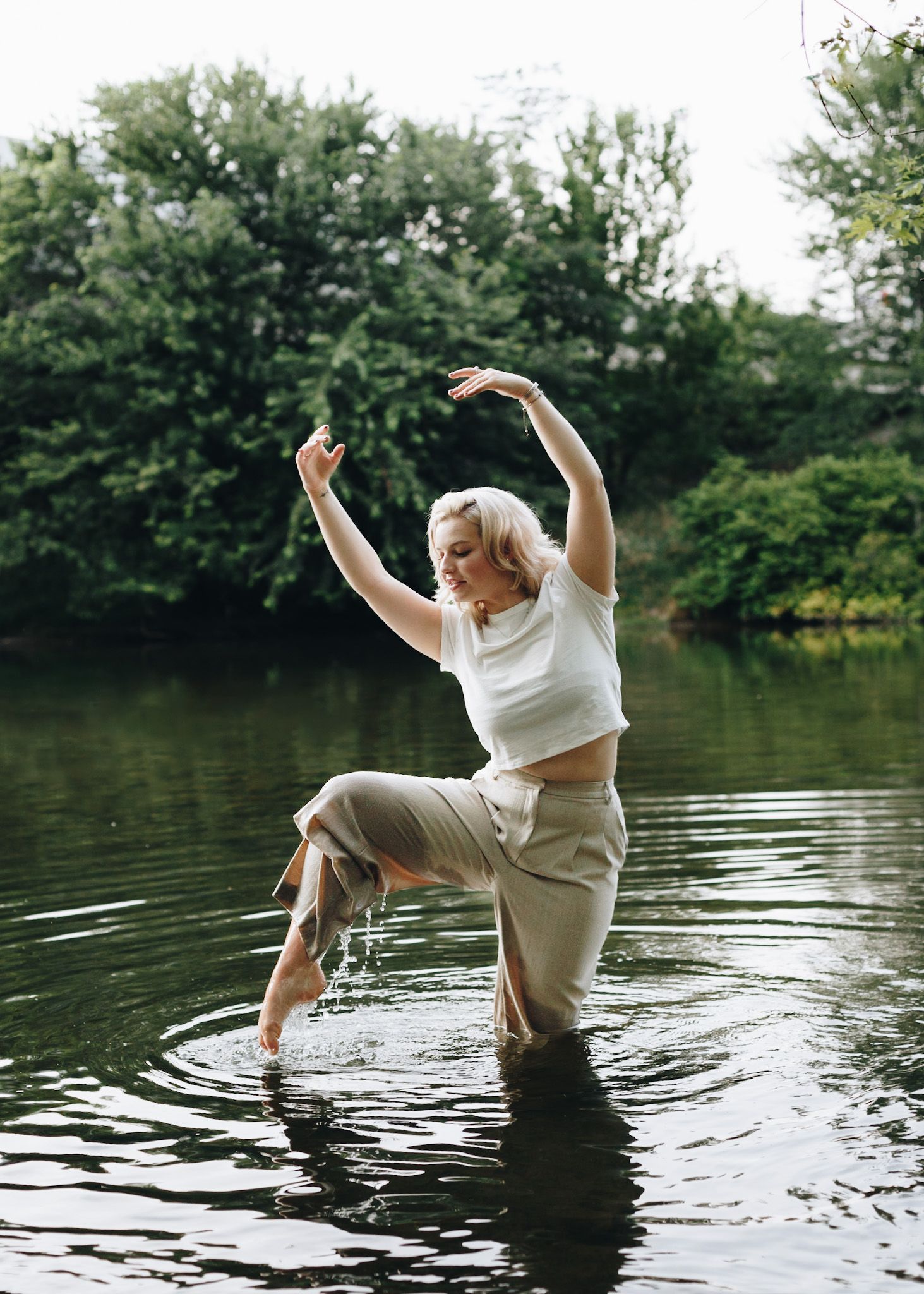 Dancer with arms raised standing in a creek near Enola