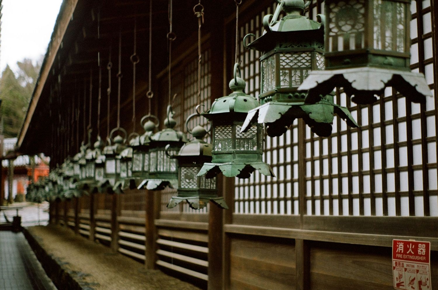 Row of traditional Japanese bronze lanterns hanging along a temple corridor.
