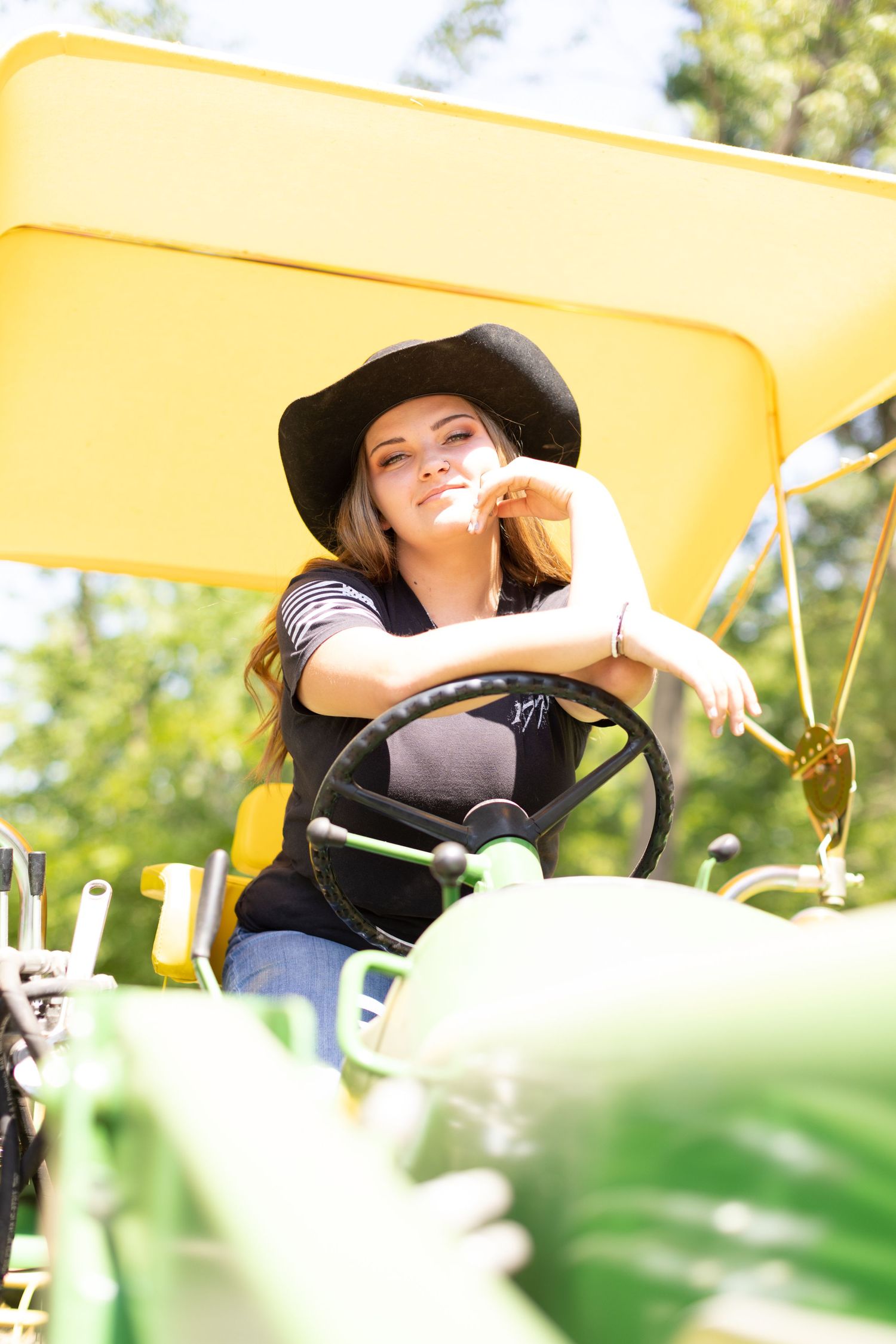 Smiling person in a black hat operating yellow farm equipment on a sunny day.