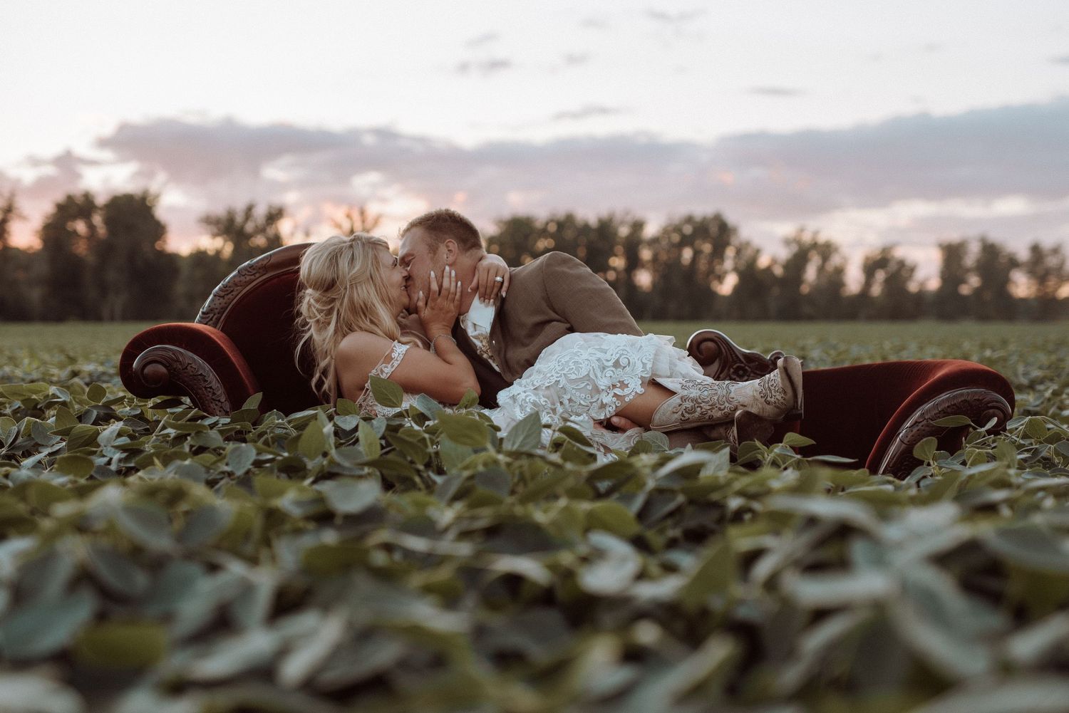 A couple lying together in a lush green garden field during sunset, with soft golden light illuminating the scene.