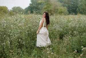 A woman in a white dress walks through a lush wildflower meadow, glancing back over her shoulder.