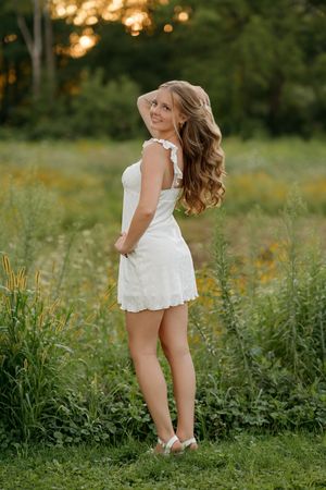 Young woman in white dress standing in a wildflower meadow at golden hour sunset.