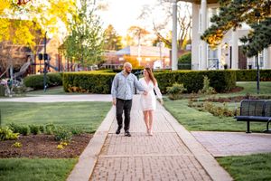 A couple walks together on a brick pathway through a garden at sunset in autumn.