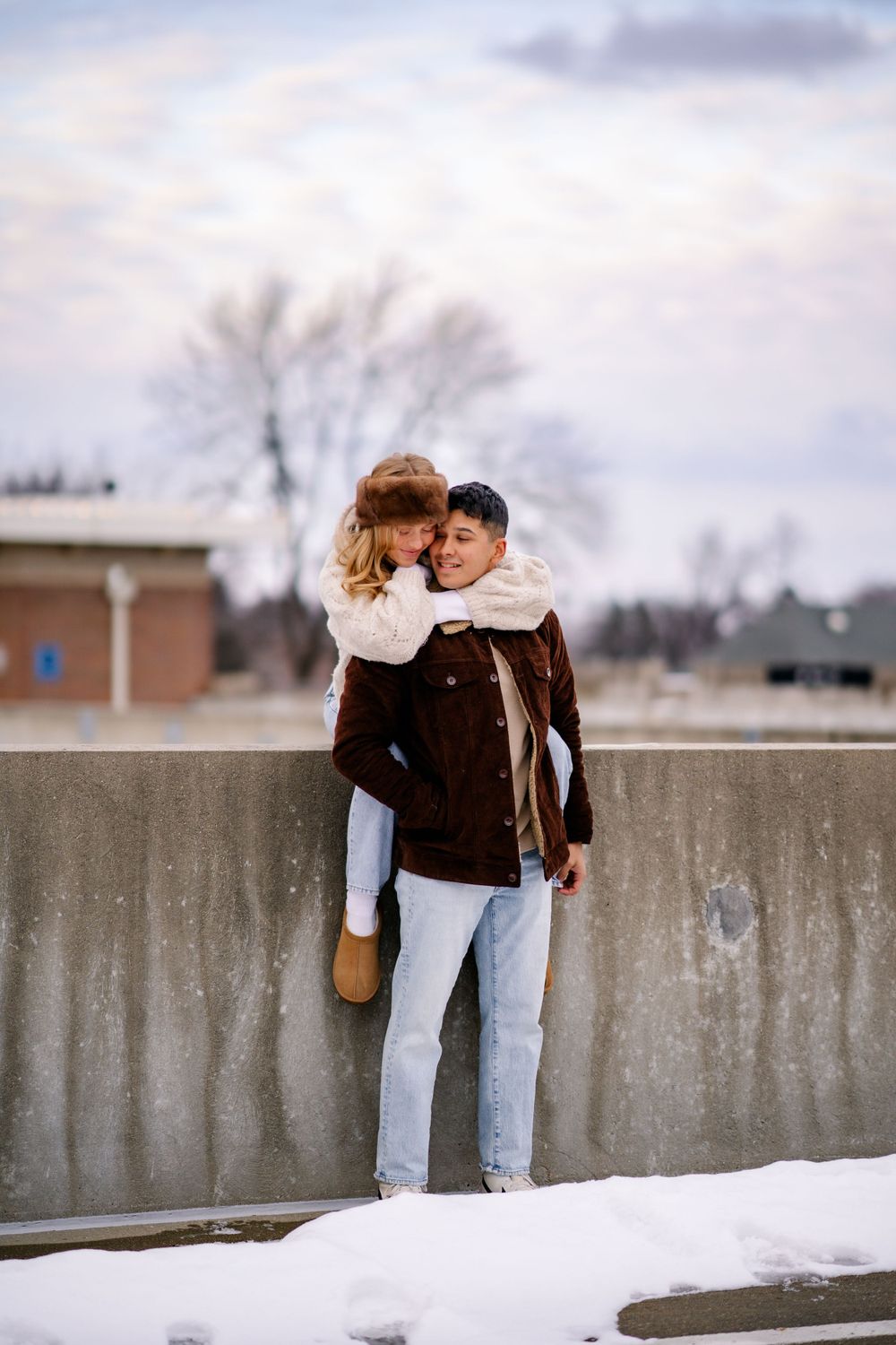 A couple sharing an intimate moment against a concrete wall in winter with light snow on the ground.