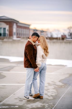 A tender moment captured between a couple in warm winter clothing standing on wet pavement at dusk.