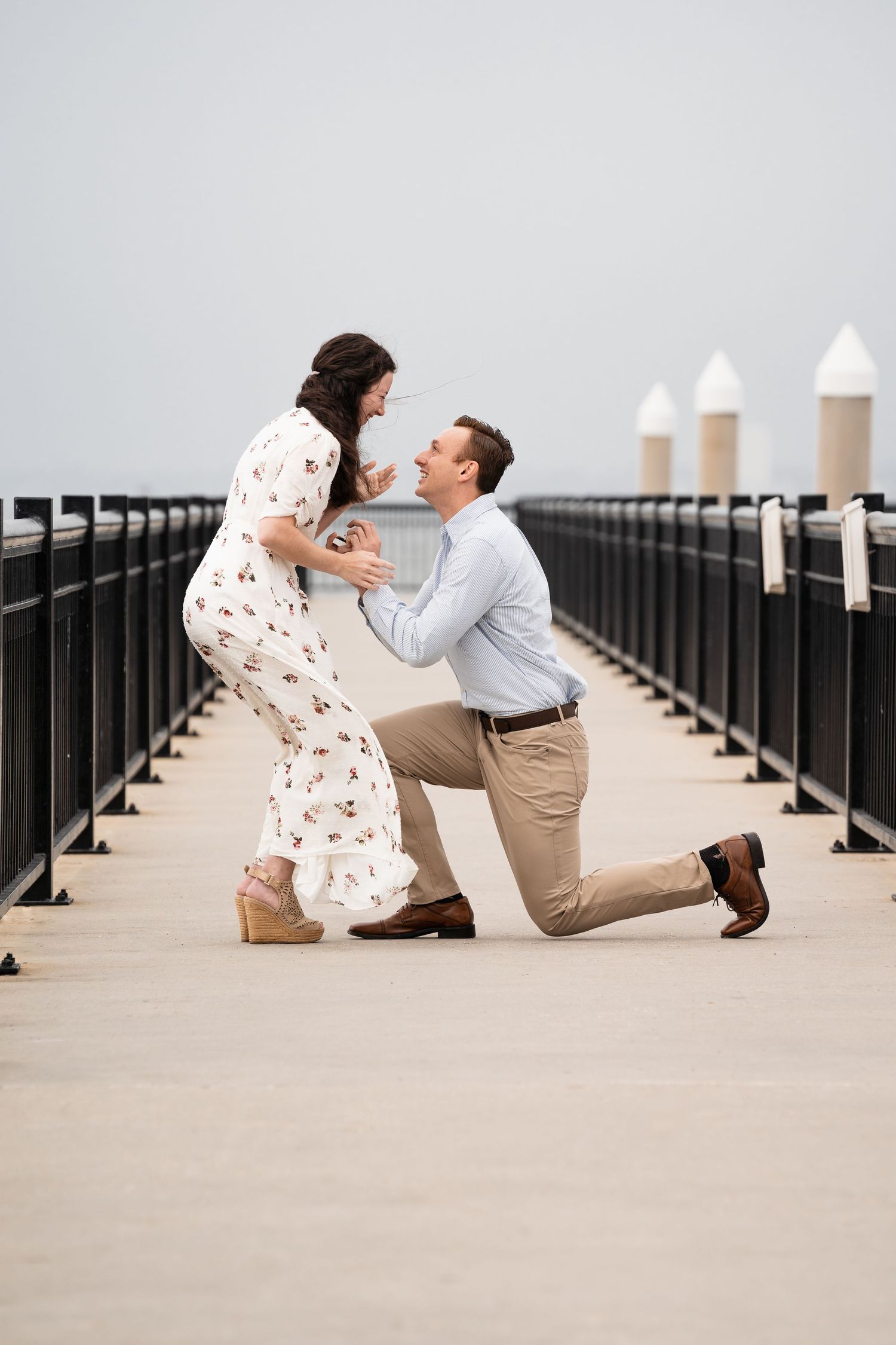 A surprise proposal moment captured on a pier with white posts.